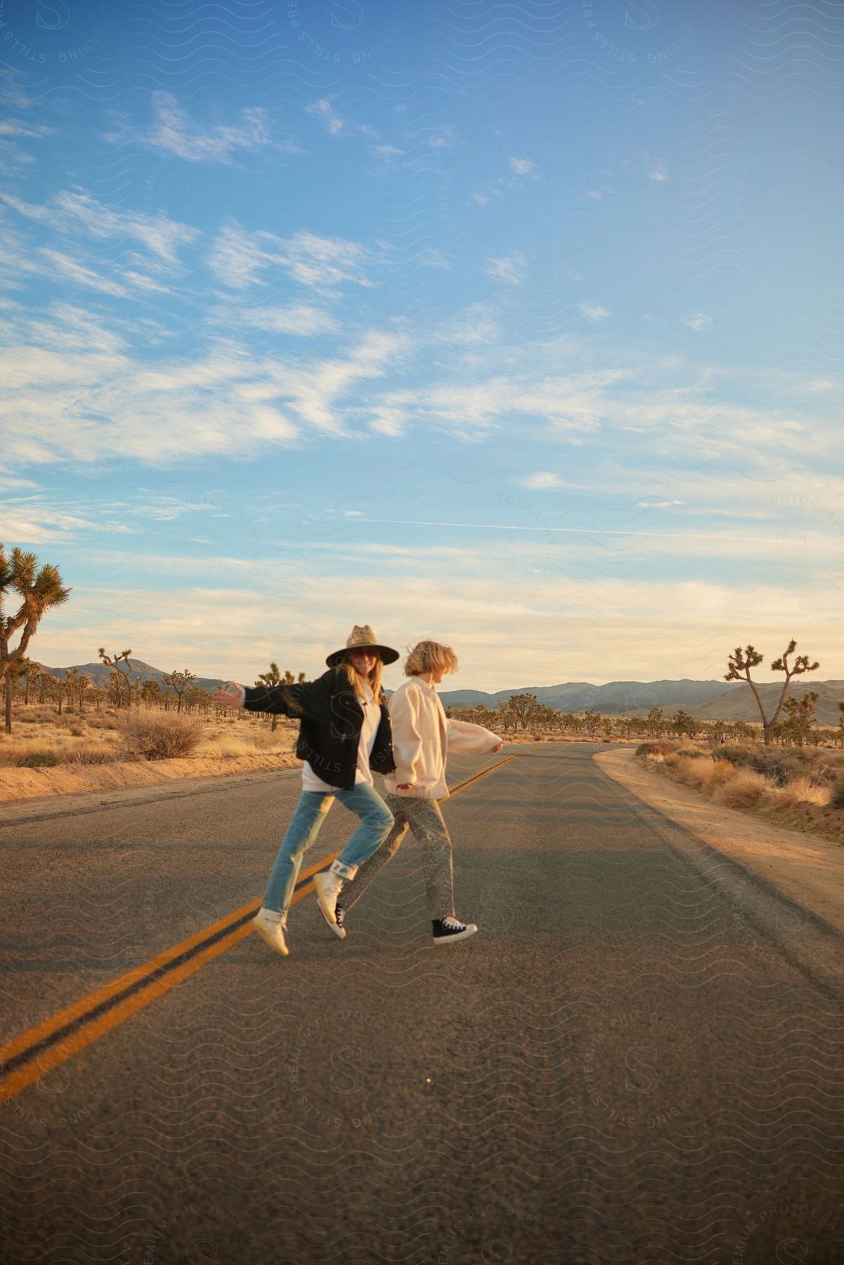 Two people walking across a desert road with mountains in the distance