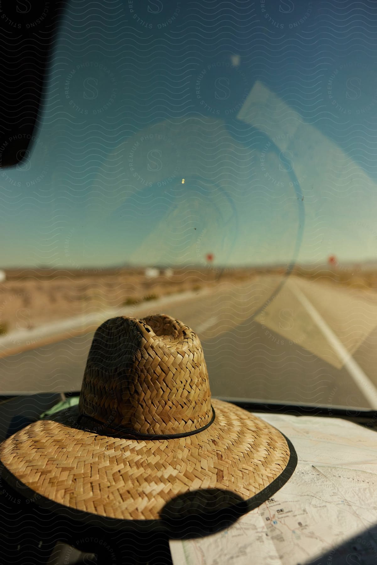 Straw hat accessory inside a car on the windshield overlooking a paved road in the middle of a deserted place.