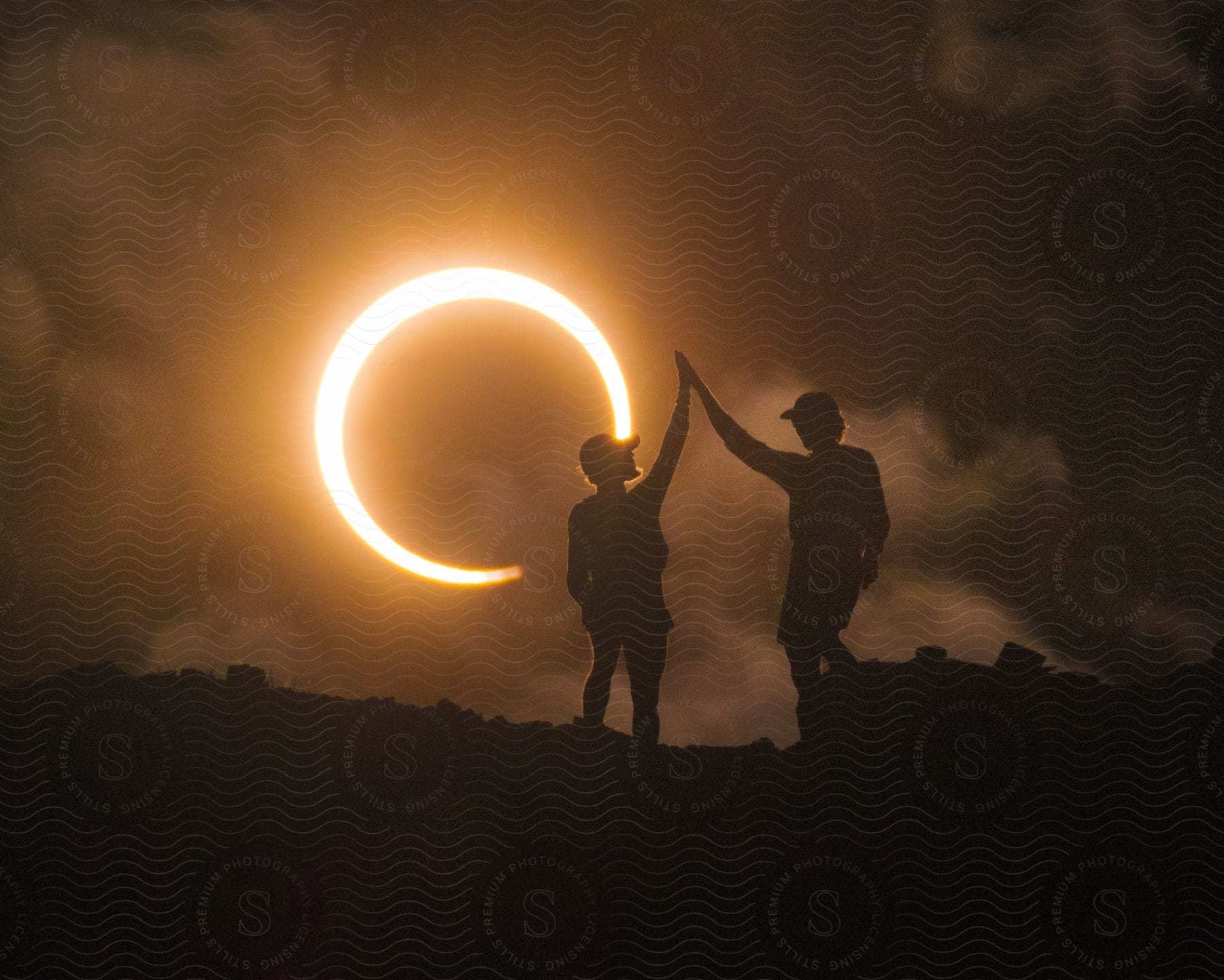 Silhouette of a man and woman touching their palms while on a mountain trail with a lunar eclipse in the background.