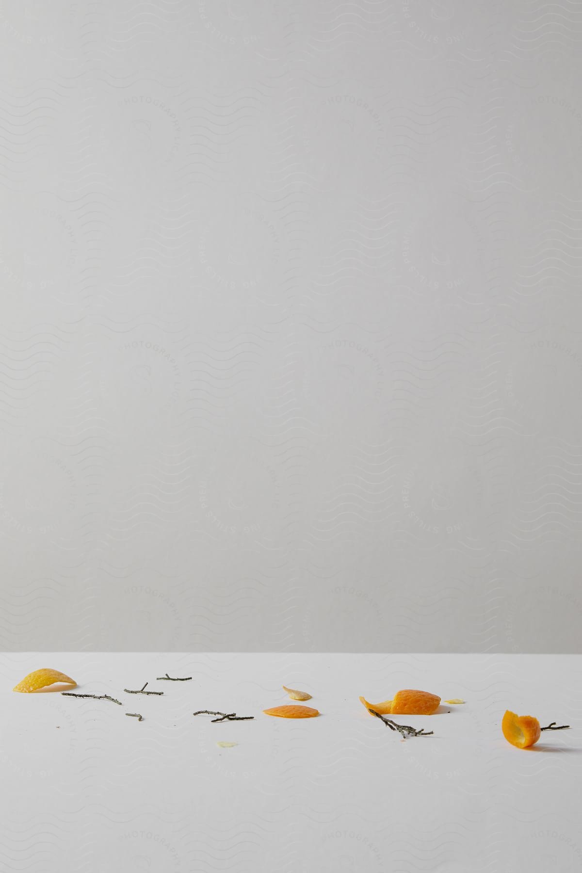 Cut orange peels and dried branches are scattered over a white surface with a light gray background, creating a minimalist and serene composition.