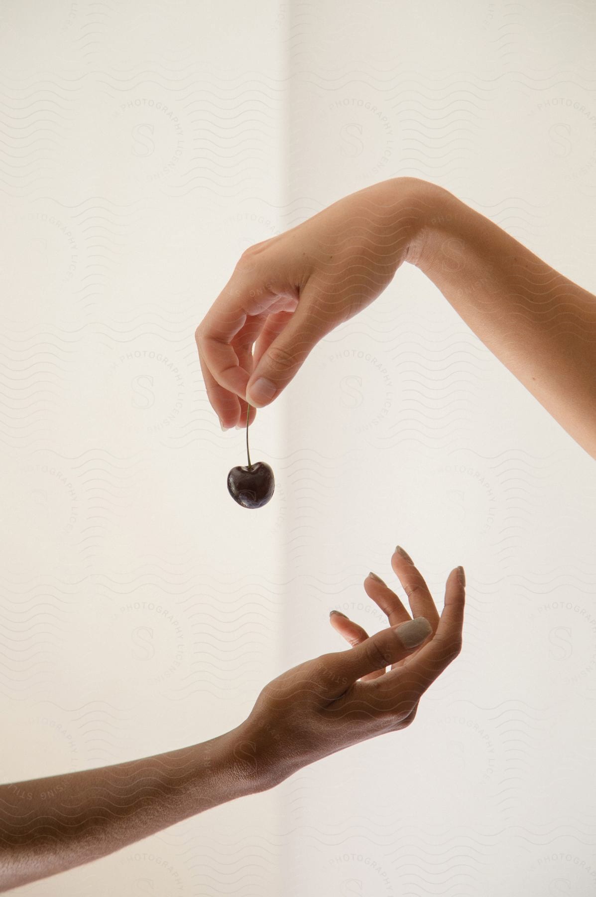 A hand passes a cherry to another hand on a white, neutral background.