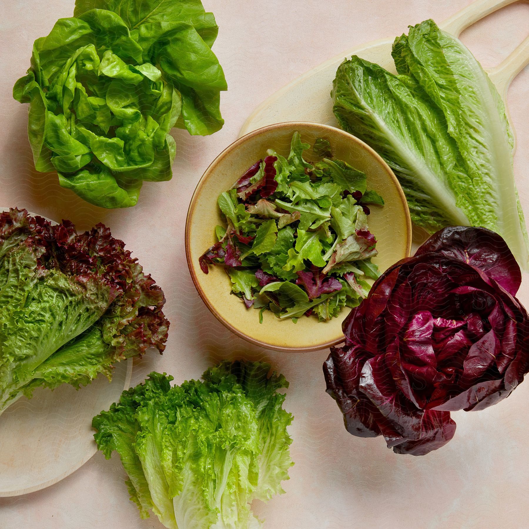 Variety of fresh lettuces including green leaf, red leaf, romaine, and butter lettuce, with mixed greens in a bowl on a light surface.