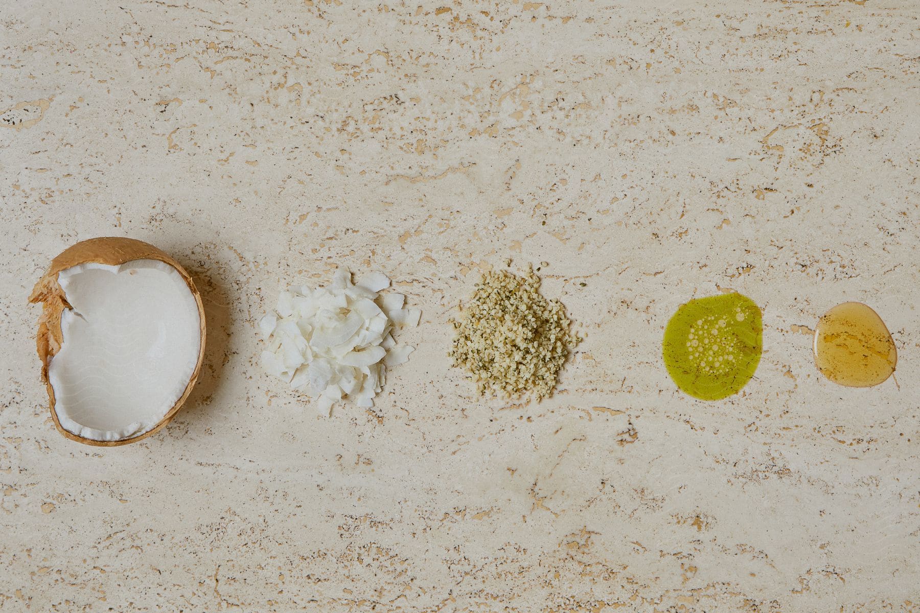 A spread of ingredients includes a cracked coconut, shaved coconut, yellow curry powder, green liquid, and an amber colored liquid.