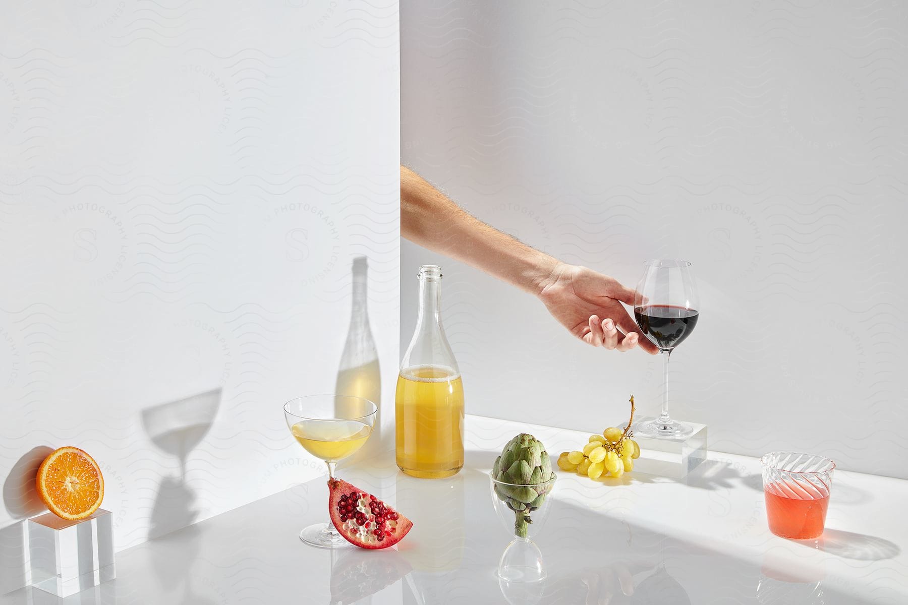Man places glass of wine into still life of produce and beverages.