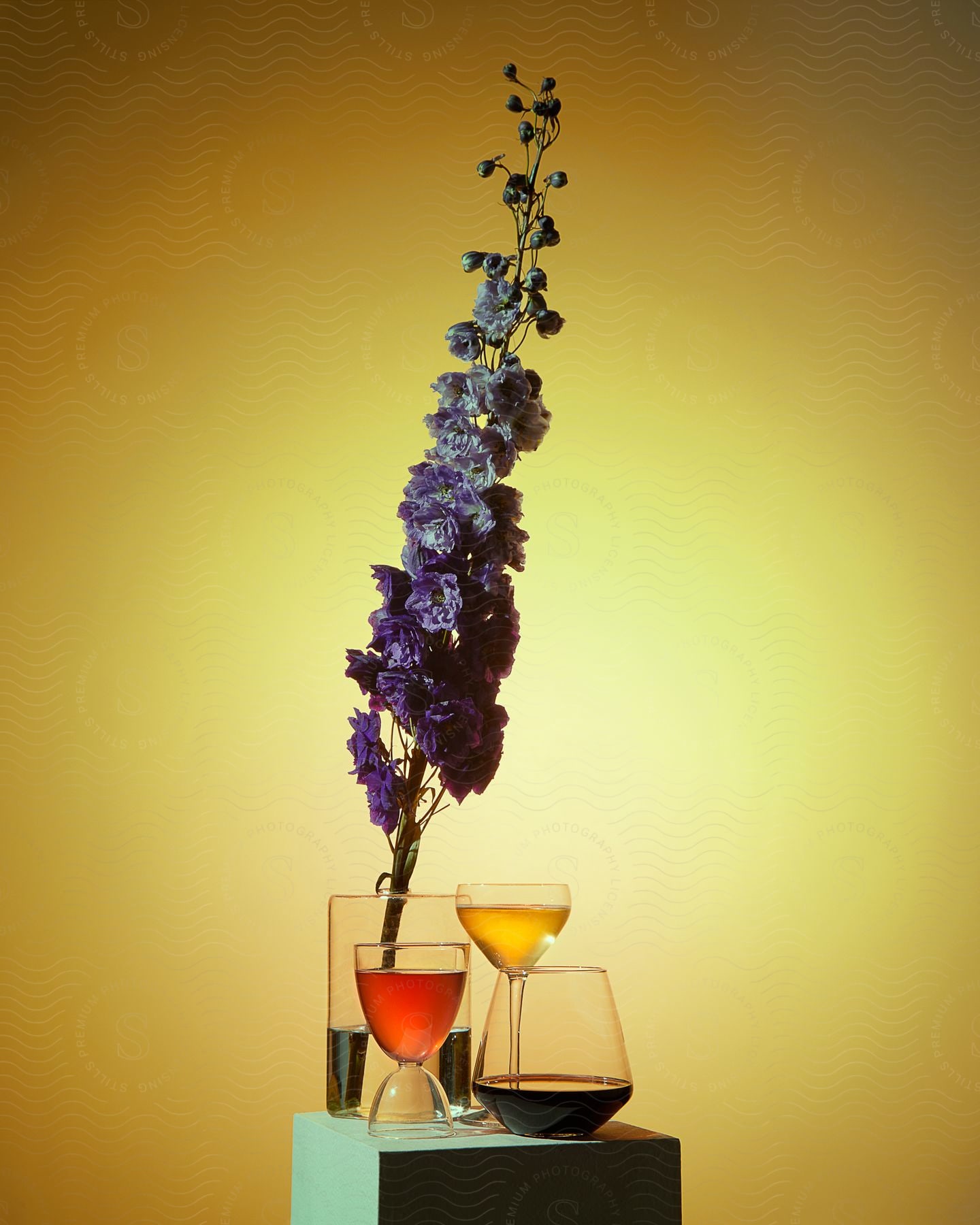 Flower in vase towers over beverages on pedestal against an amber room.