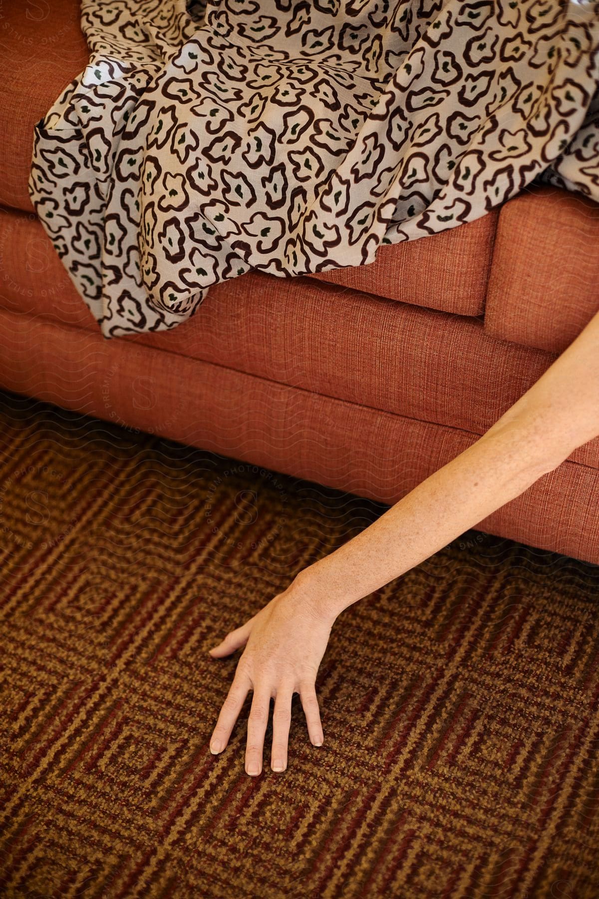 A person's hand under a rug lying on a red sofa, reaching the floor.