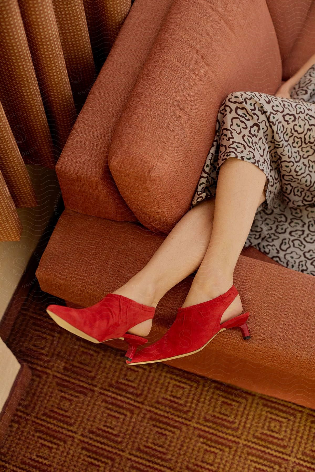 Close-up of the legs of a woman in a dress lying on an orange sofa and wearing red high heels