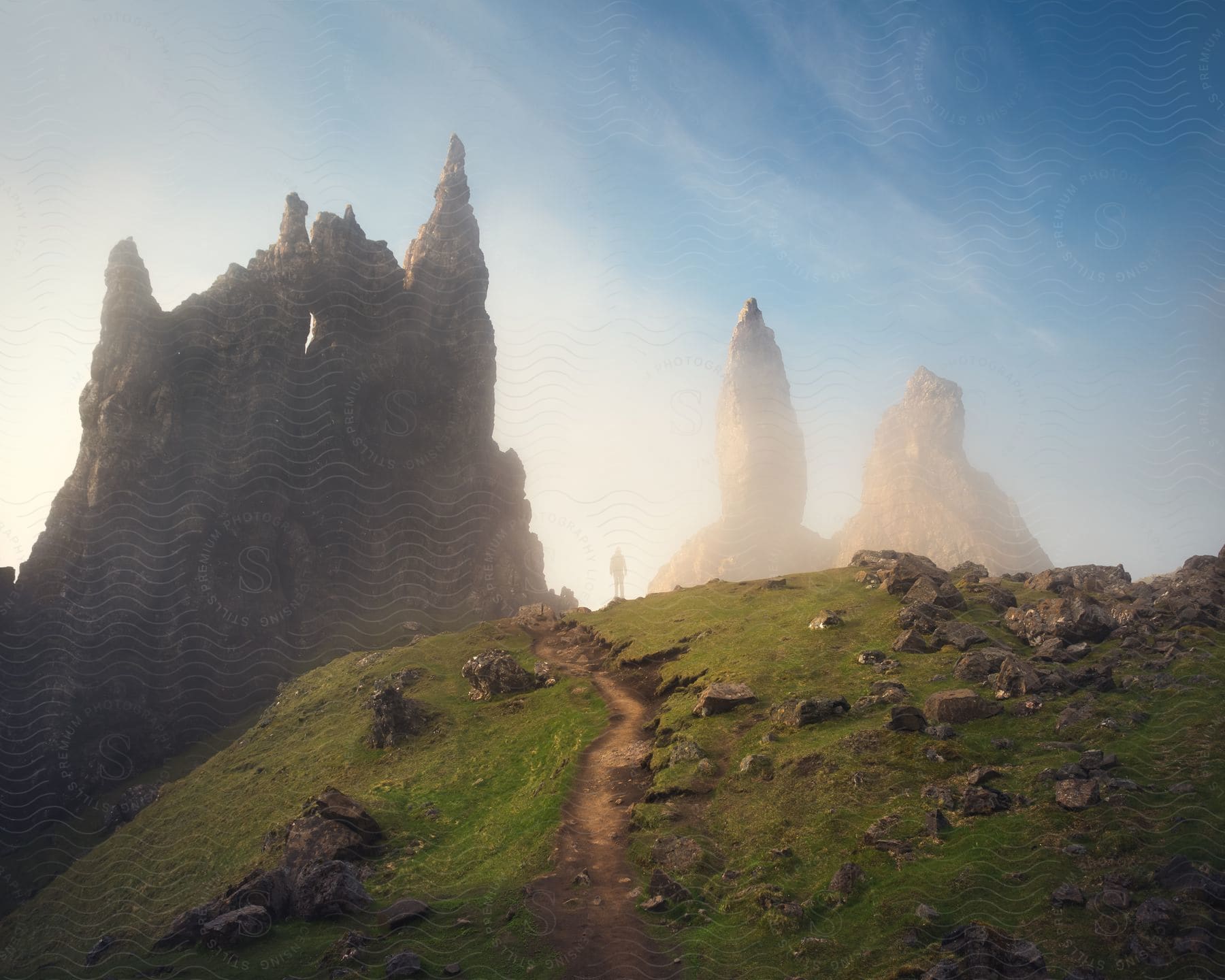 Silhouette Of A Person Walking Towards Imposing Rock Formations Amid A Mysterious And Foggy Landscape