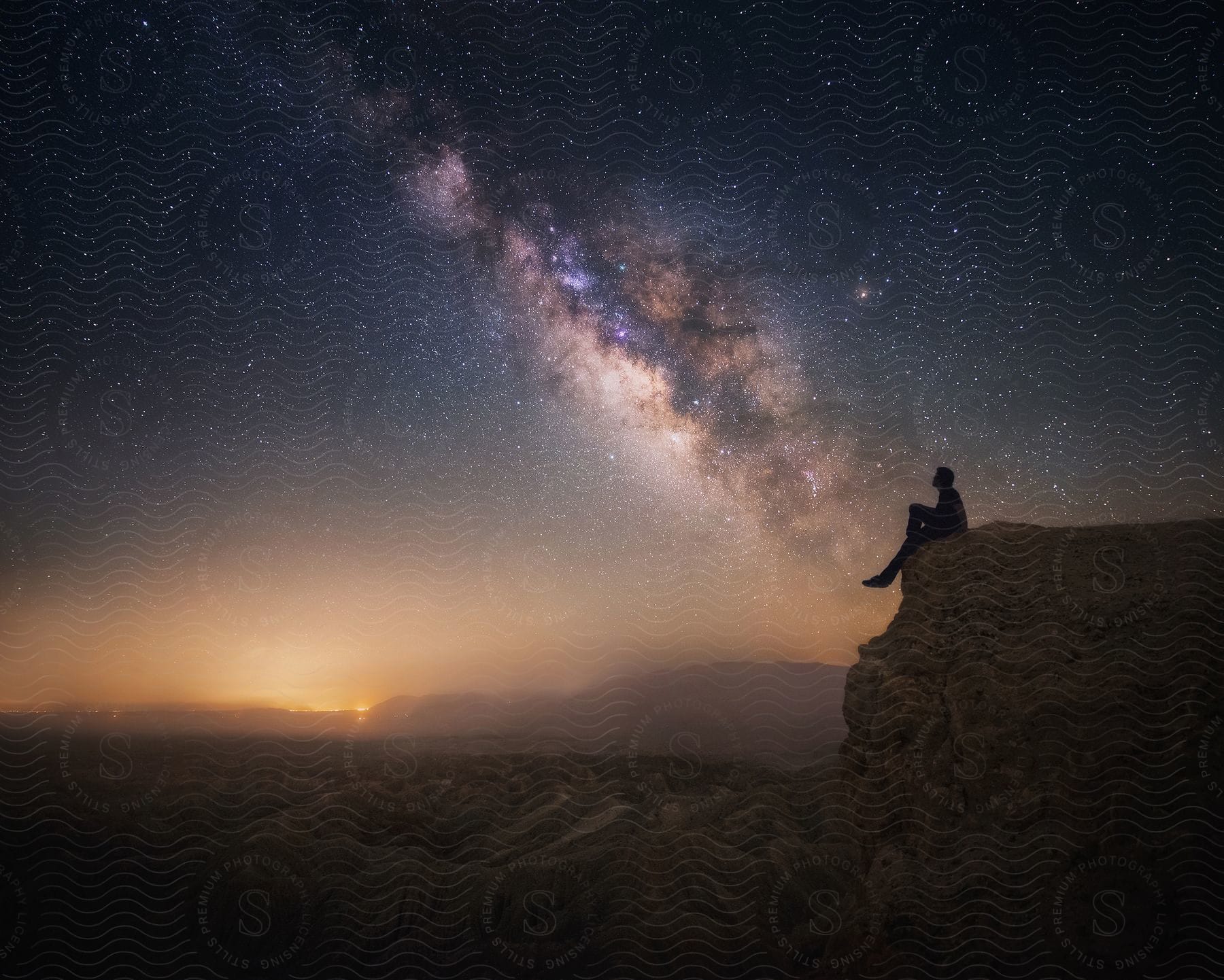 A man views the Milky Way just as the sun sets beyond the sandy mountain in the desert.