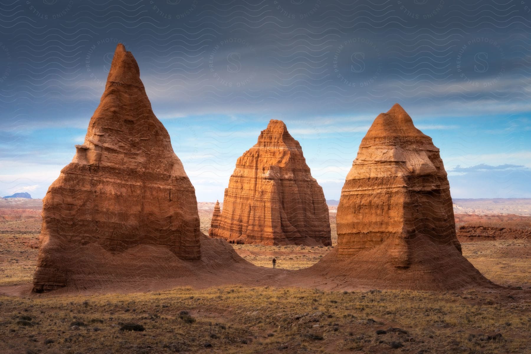 A person stands between three giant rocks in a desert on a mostly cloudy day.