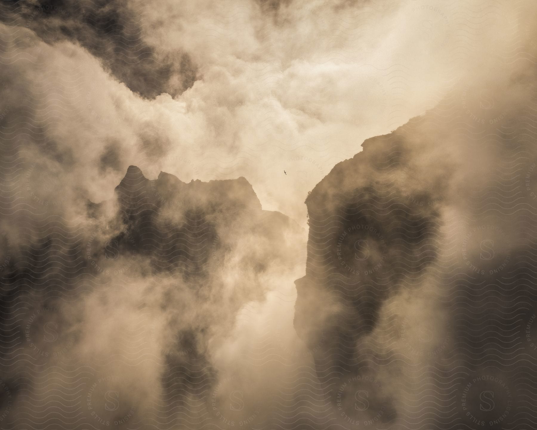 Fog envelops the atmosphere around a mountain or rocks at sundown, creating a golden atmospheric condition.