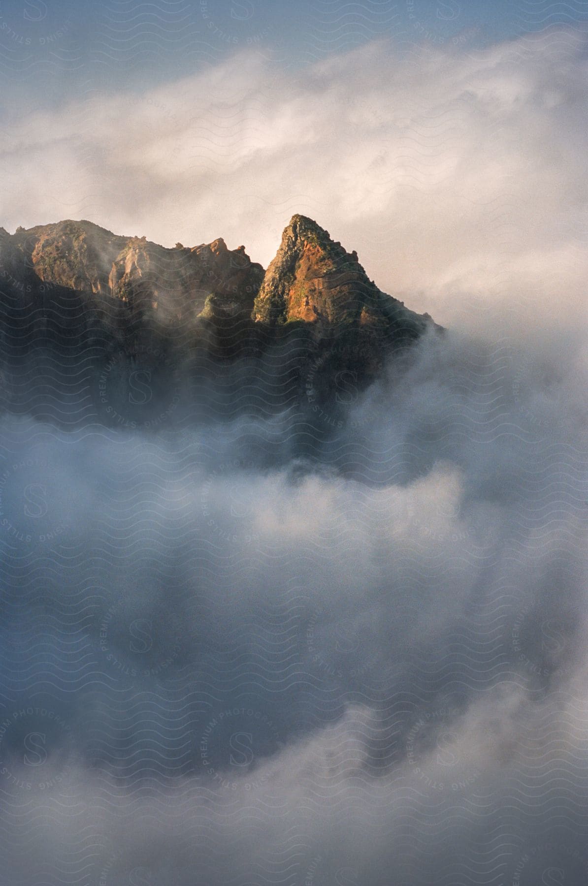 Fog envelops the atmosphere surrounding a mountain on a sunny day.