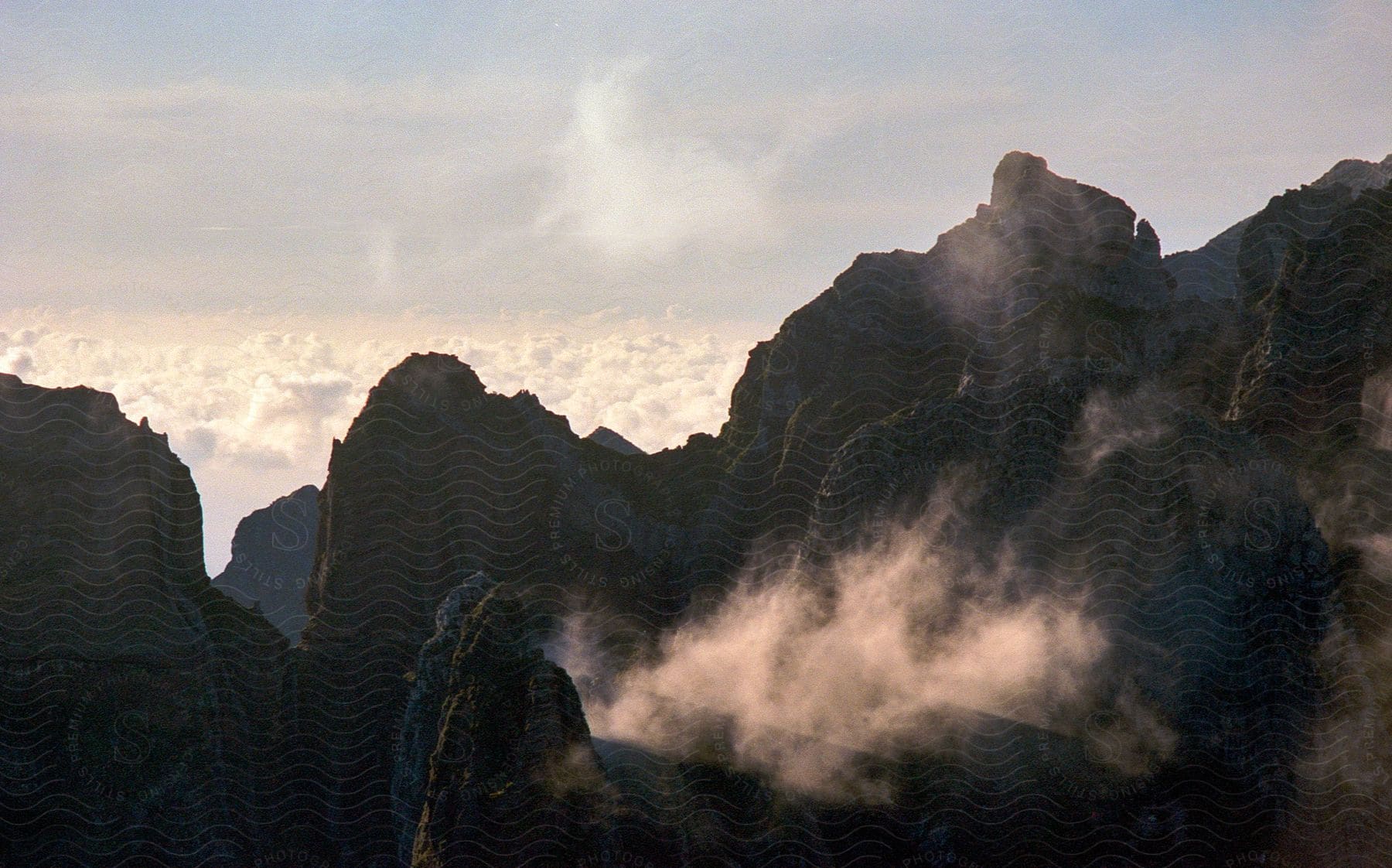 A majestic scene of a cloudy rocky mountain range under a cloudy sky. Mist hangs over the mountains, creating a mysterious and imposing atmosphere.