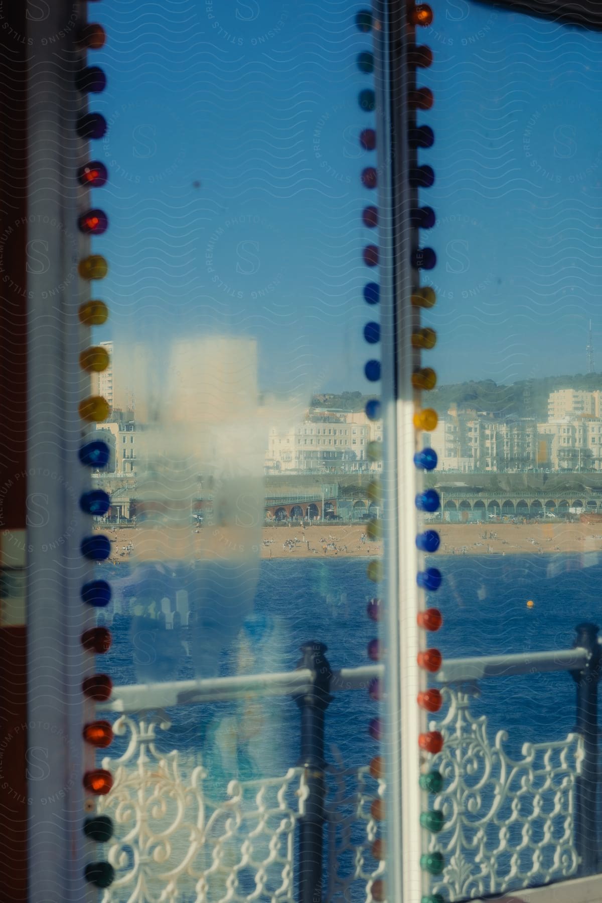 A glass window with several colored dots and it is reflecting a beach with a very blue sea and people on the sand