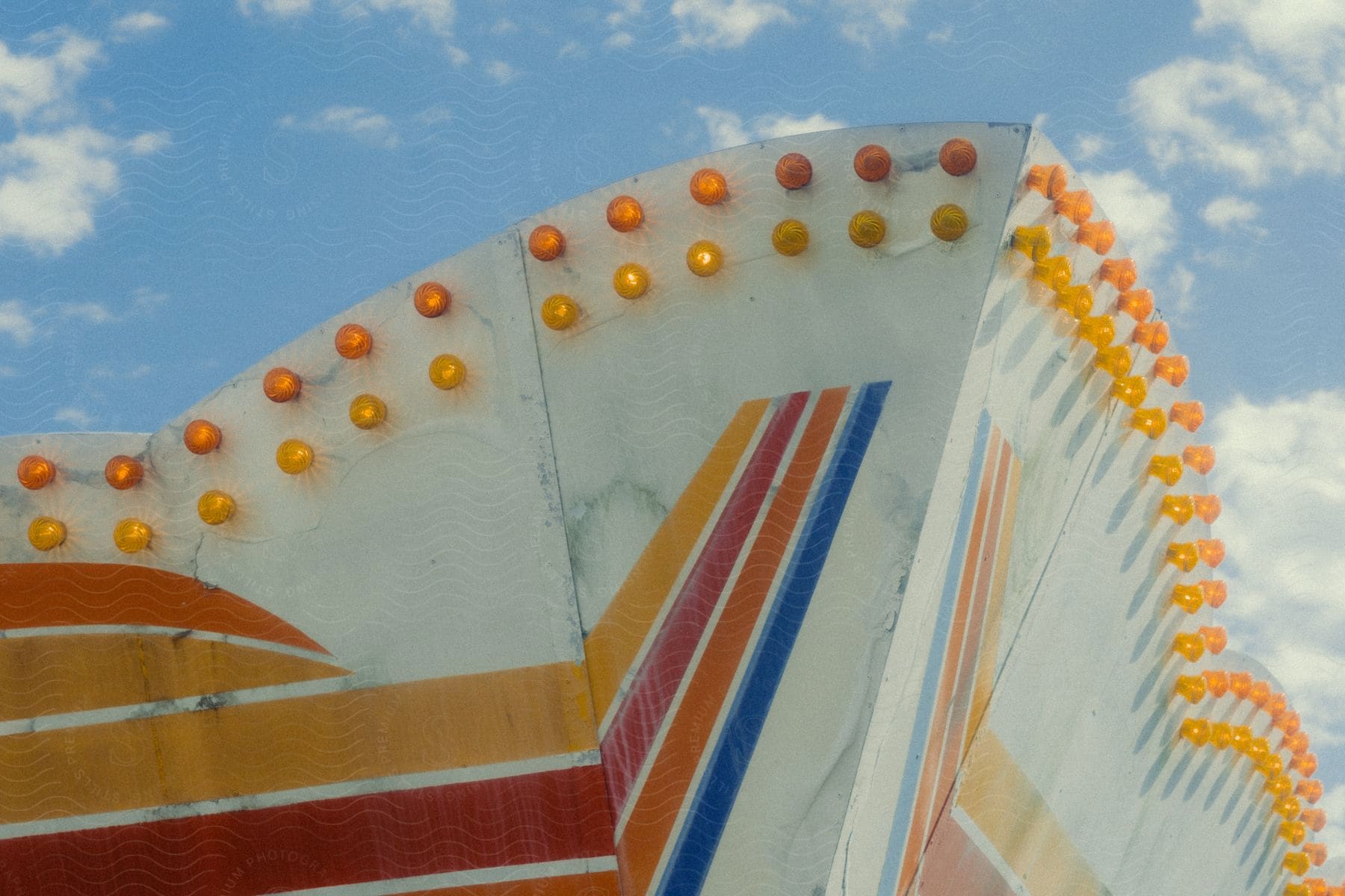 The roof surface of an amusement park is painted in stripes of yellow, red, orange, and blue, with lots of small yellow lights at the top.