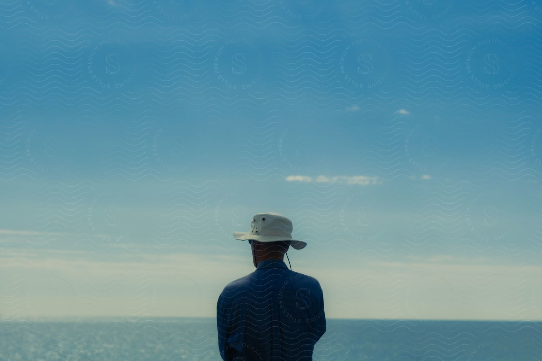 Man in a hat gazes at the ocean.