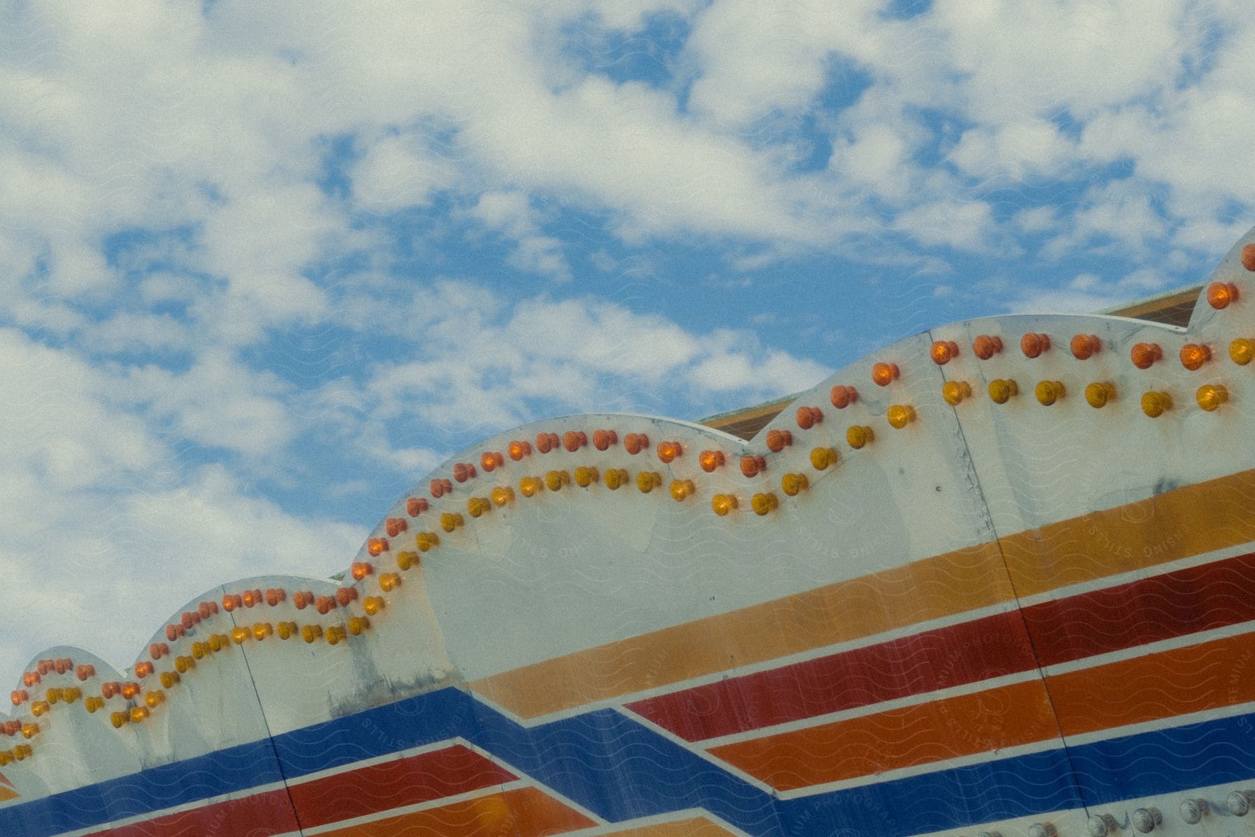 Close-up on the exterior architecture of a metal amusement park ride and flashing lights during a blue sky day with clouds.