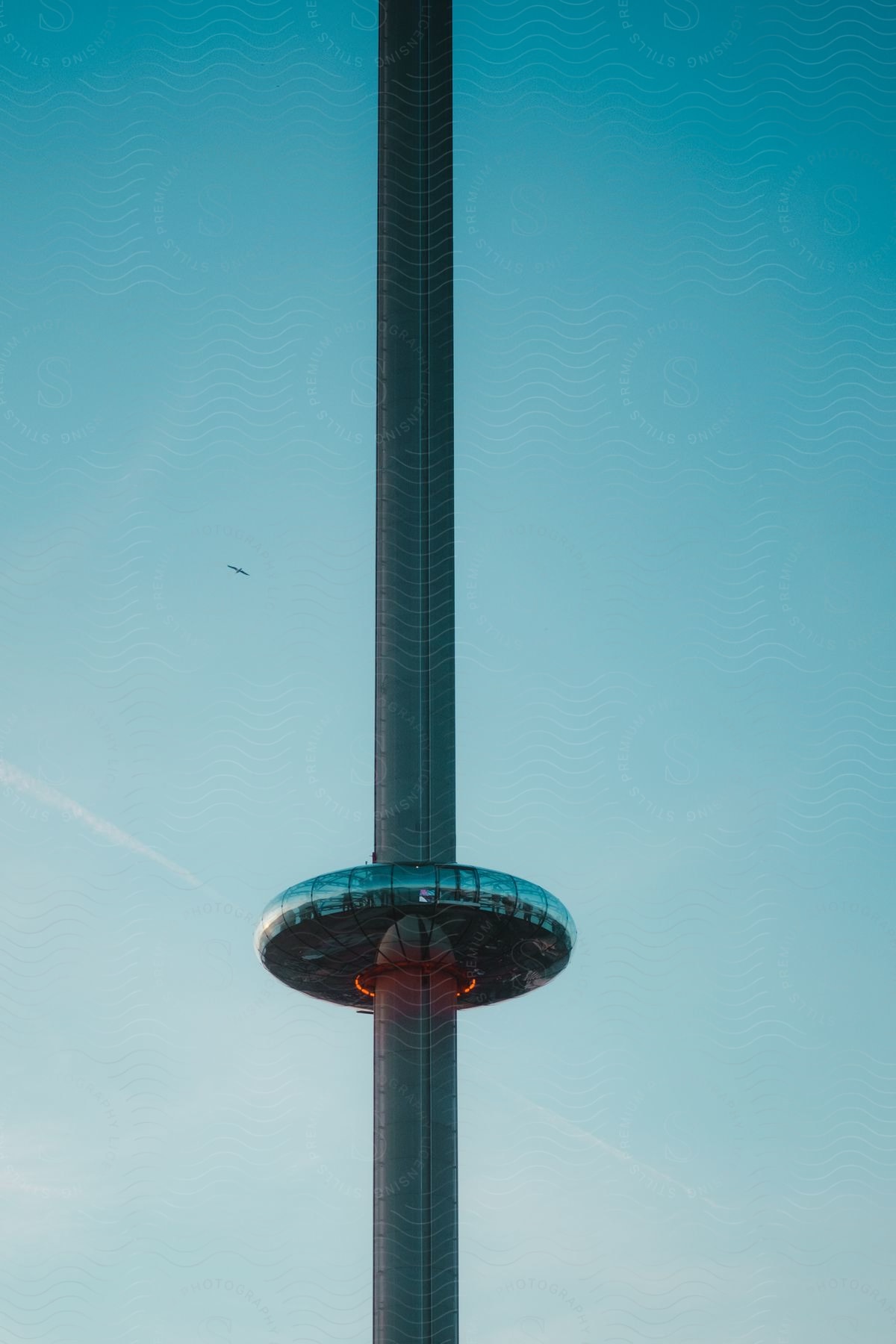 Tall observation tower with a circular viewing platform against a clear blue sky, with a small bird flying nearby.