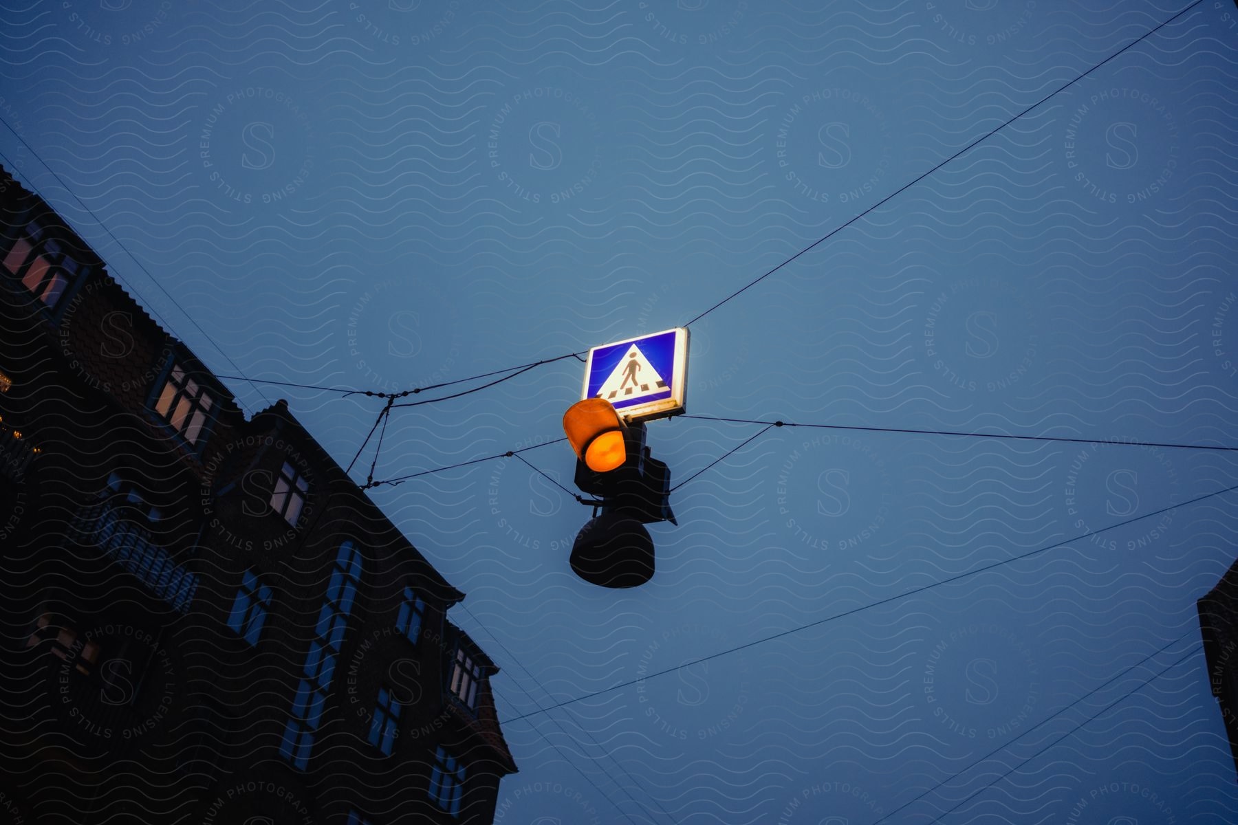 Traffic light hanging by wires in a city and the silhouette of a building next to it on a dark sky day.