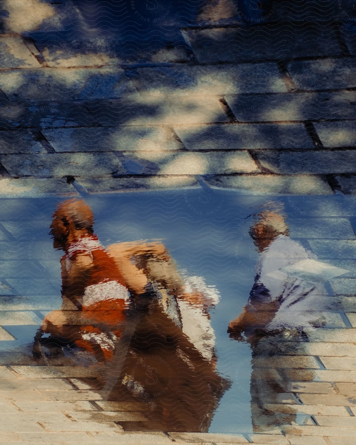 The distorted reflection of people in a pool of water on a brick floor, creating an intriguing mix of textures and shapes.