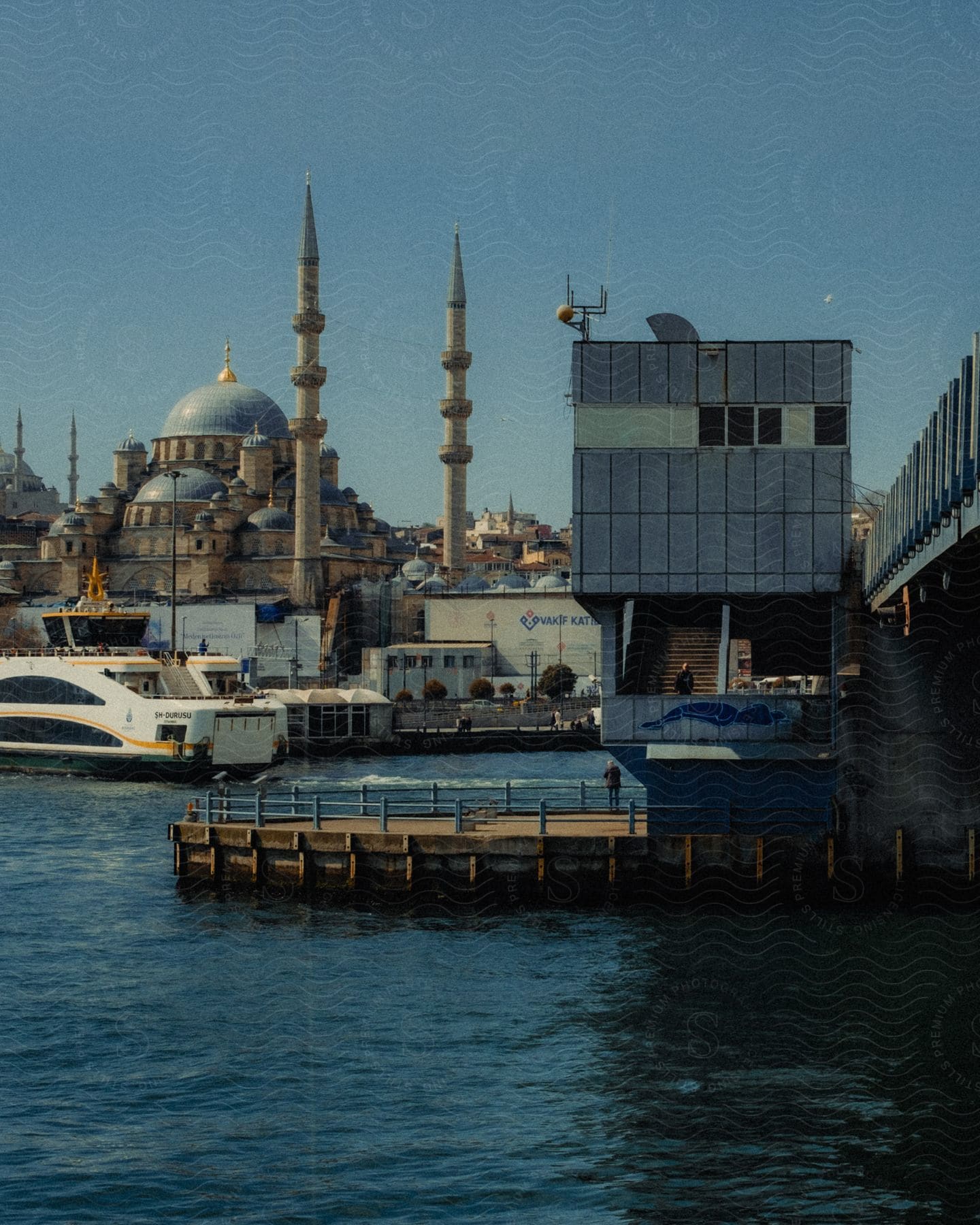 Waterfront view with a mosque in the background and ferry dock in the foreground under a clear sky.