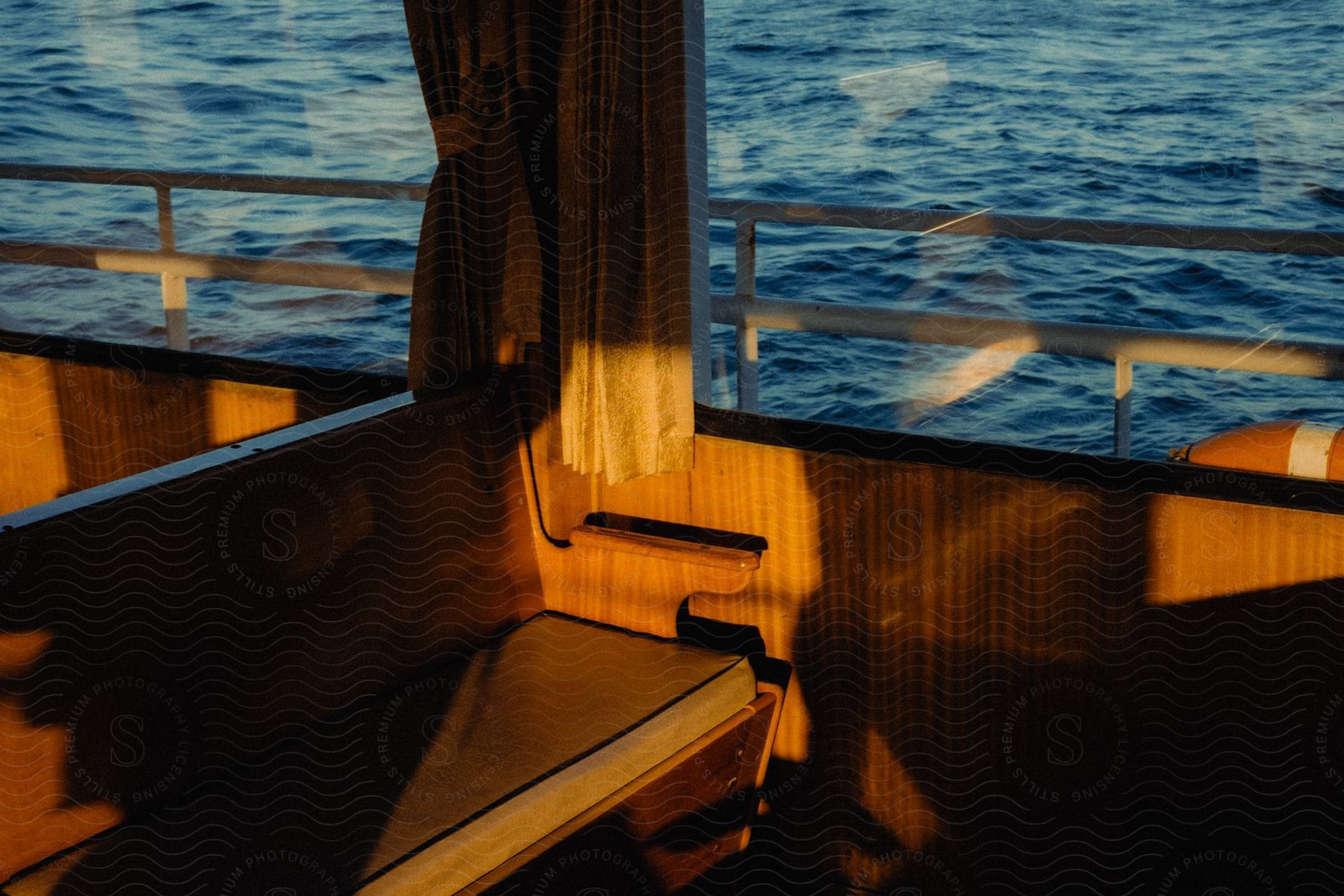 Interior architecture of wooden benches of a boat with windows overlooking the sea and the reflection of sunlight.