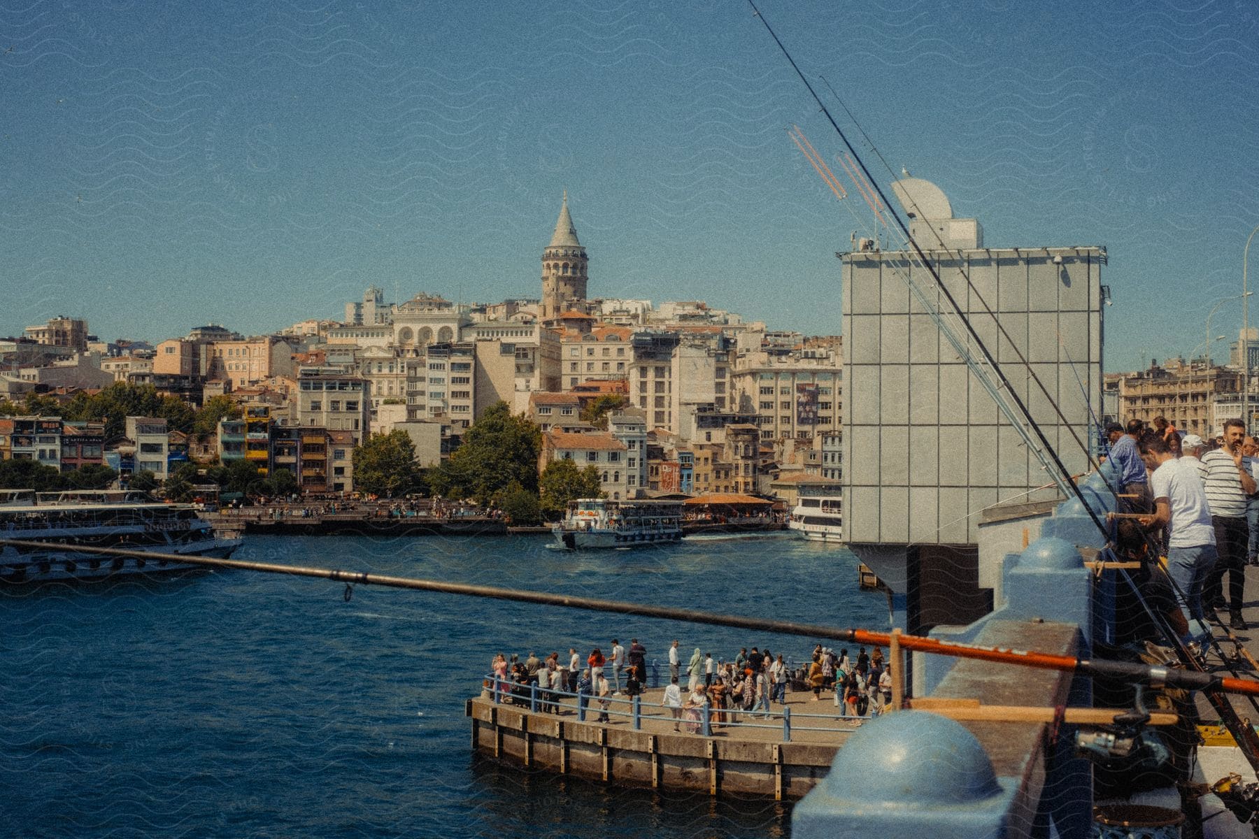 A Pier with several people in front of a Bahia and at the top there are people with fishing rods pointed at the water