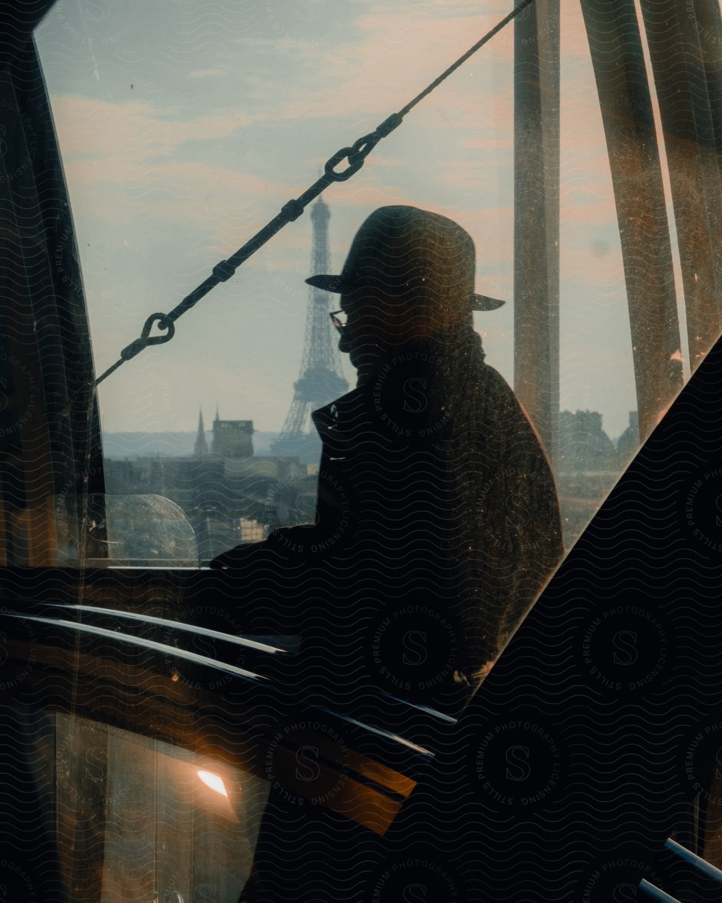 A person's silhouette is seen through a window with the Eiffel Tower in the background, creating a contemplative and serene setting in Paris.