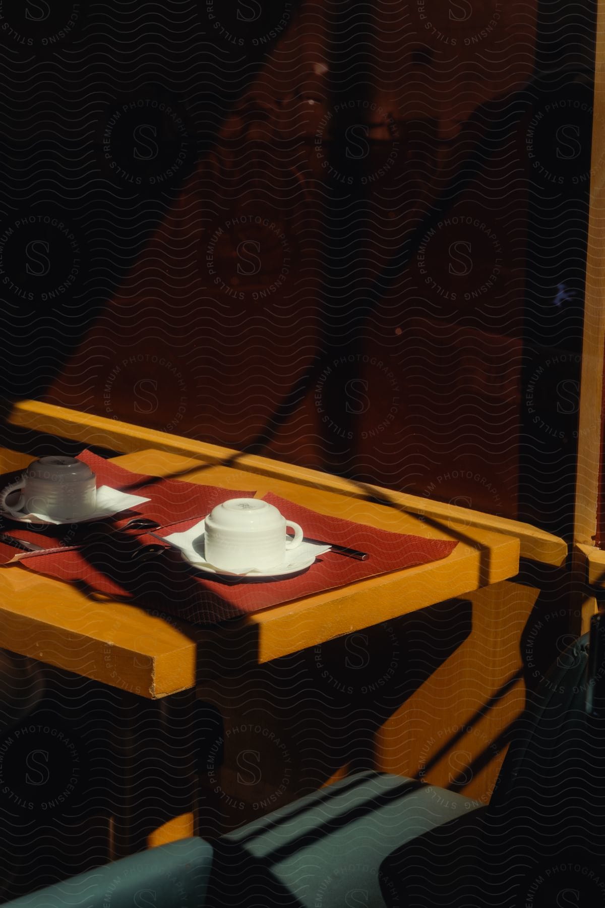 A wooden table with two cloths and two white cups on top and next to a glass window