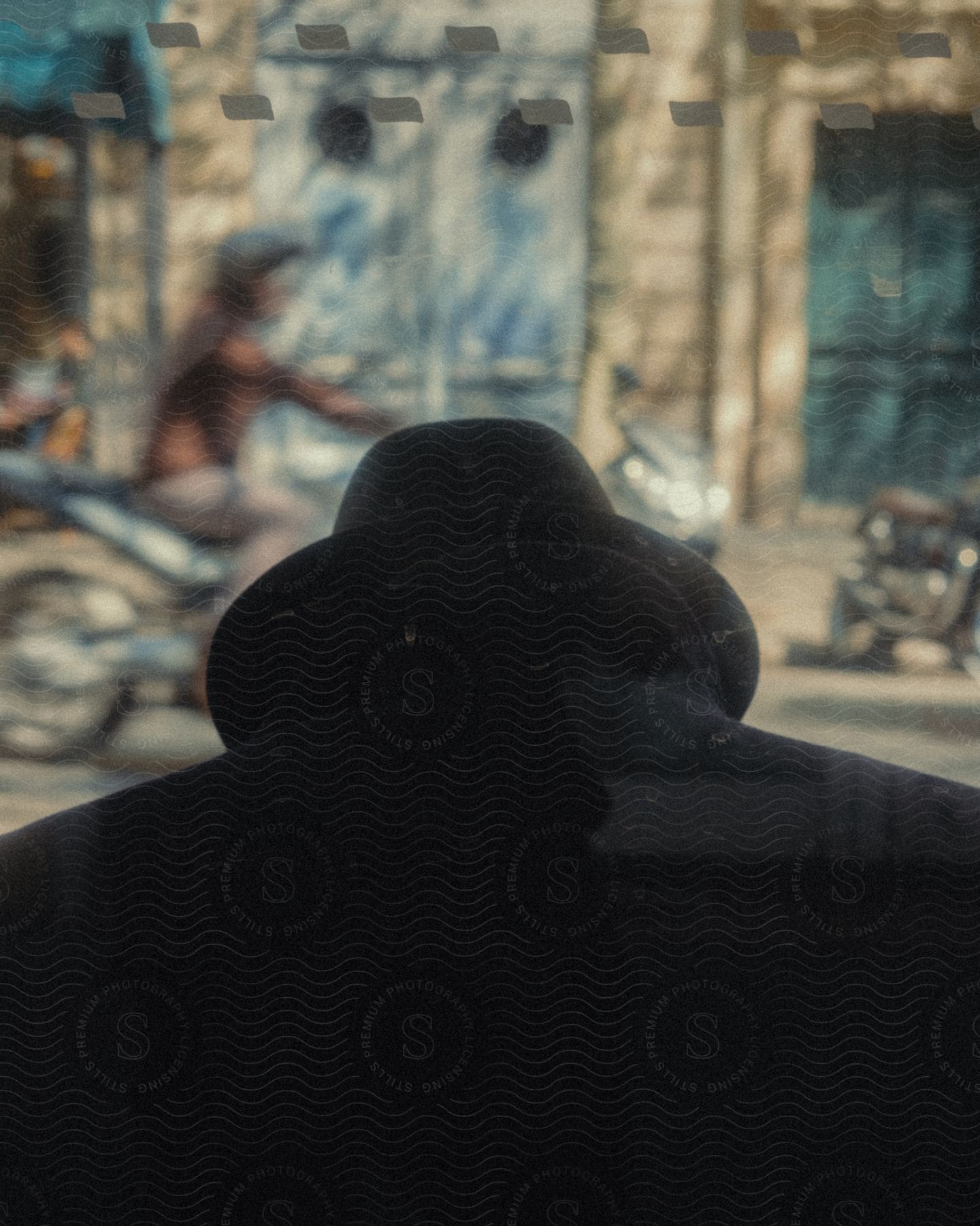 A man with dark coat and hat with his head low on a city street as people pass him by.