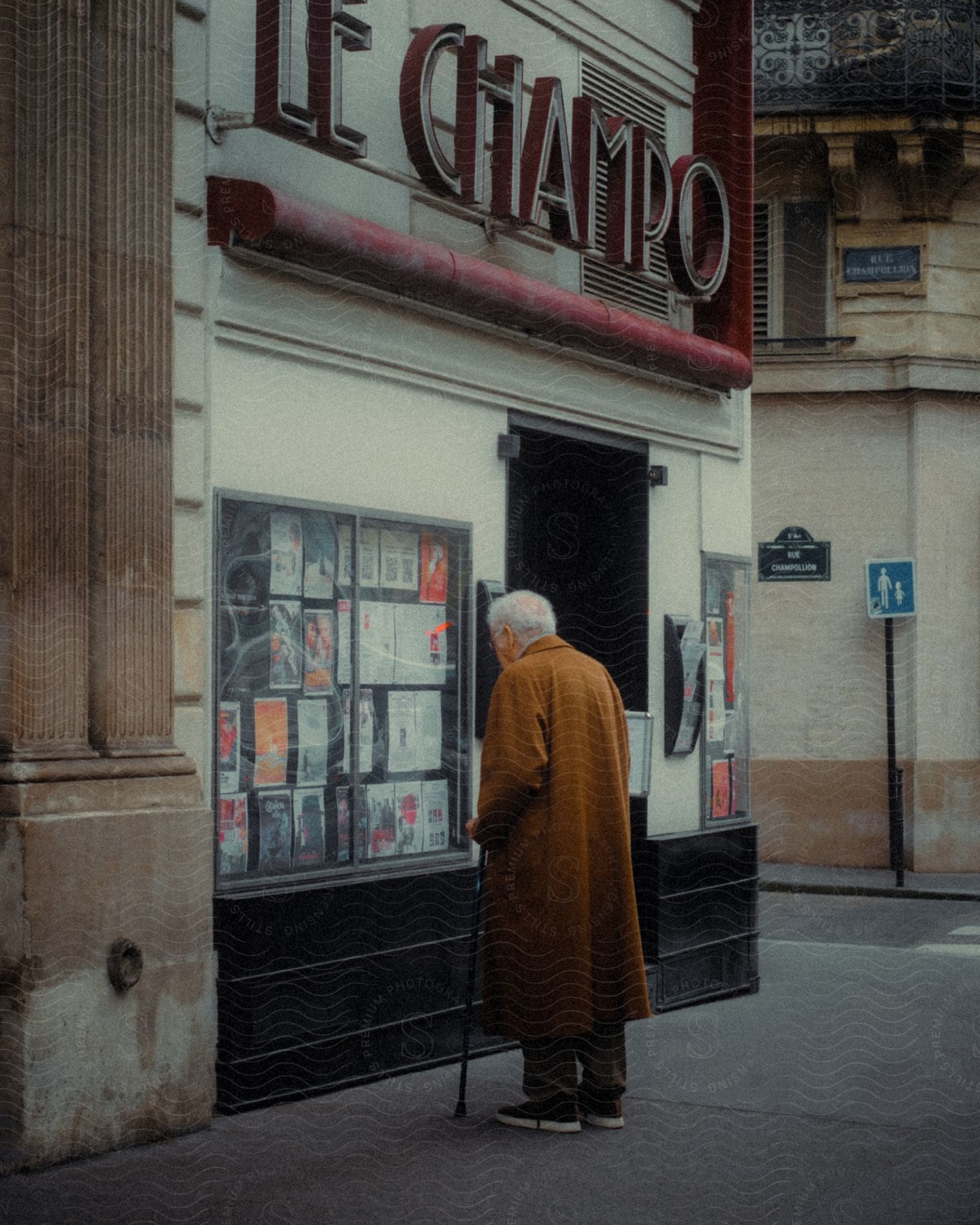 An old man stands in front of a shop window looking at posters