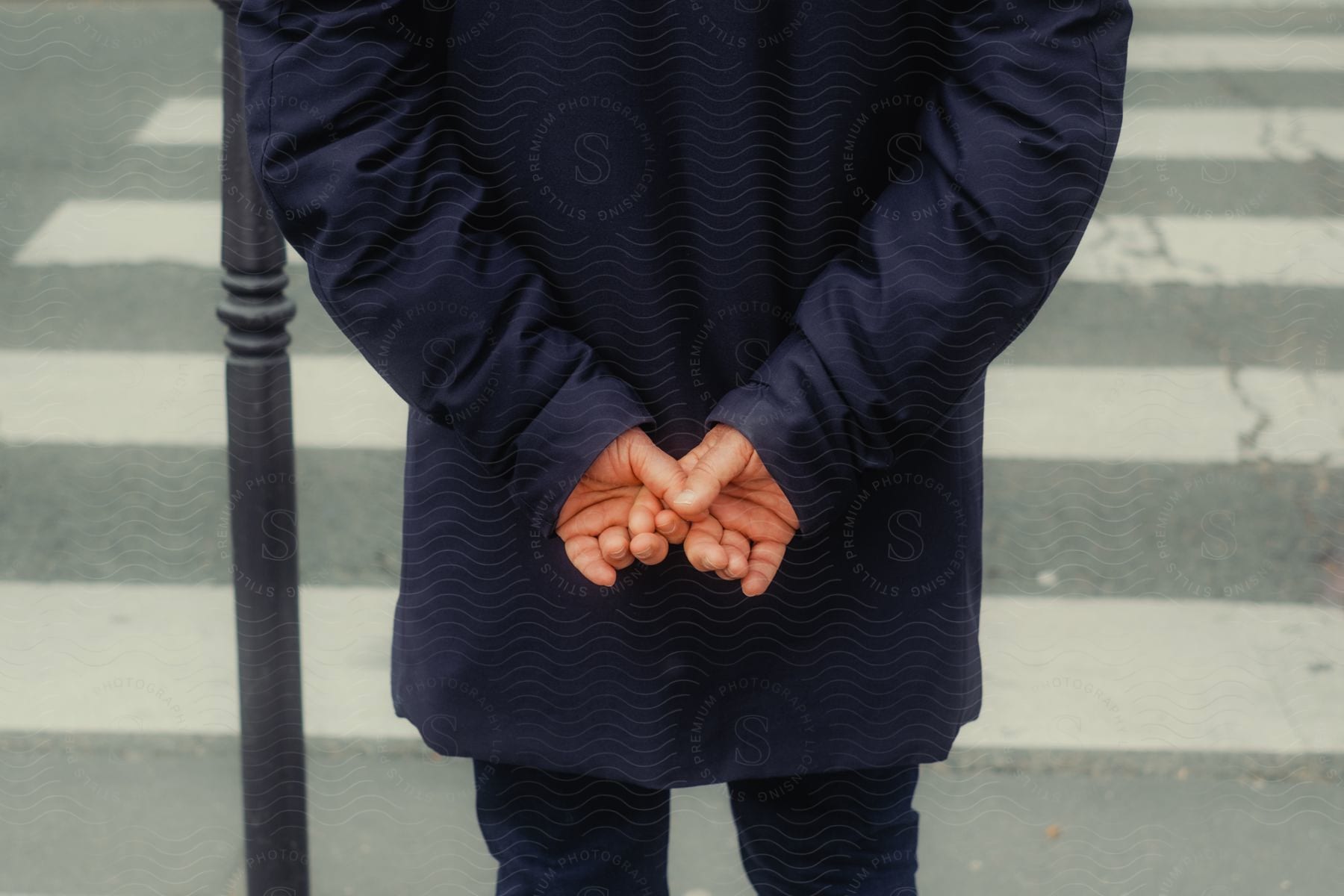 Close-up of a person's clasped hands from behind, wearing a long-sleeved blouse and in front of a crosswalk.