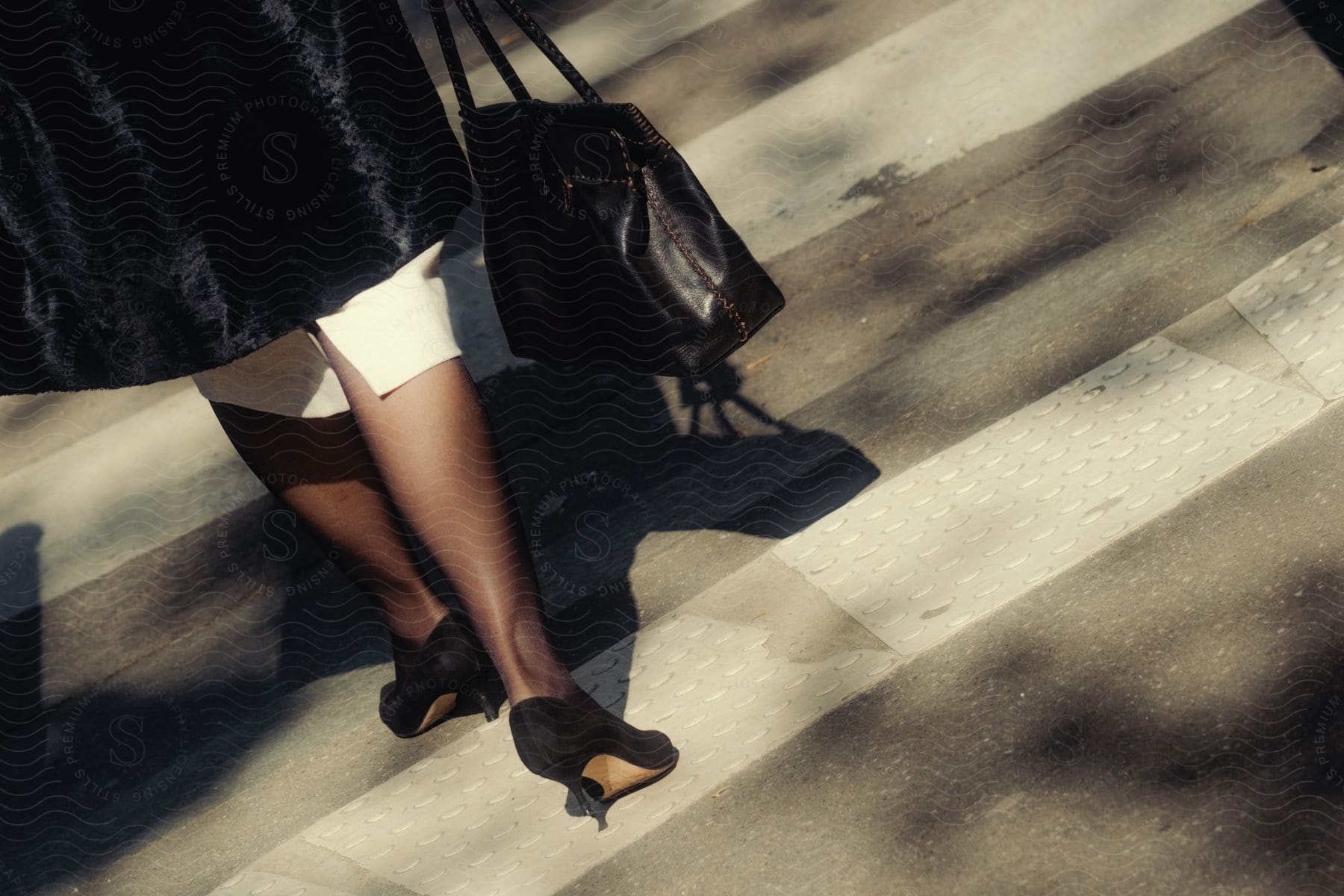 Close-up of a woman's legs crossing a pedestrian crossing holding a leather bag and walking in high heels.