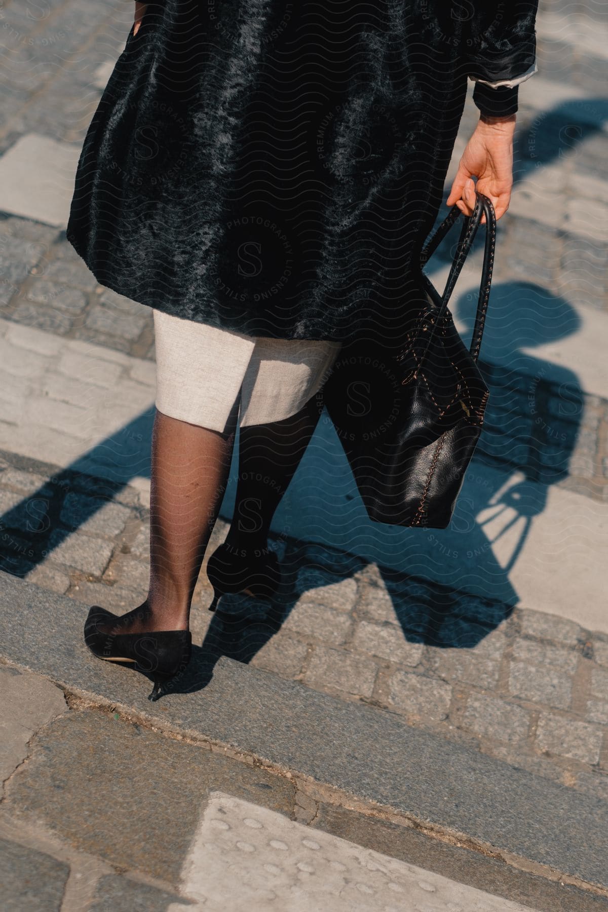 A woman holding a purse and crossing a crosswalk, her shadow falling on the road