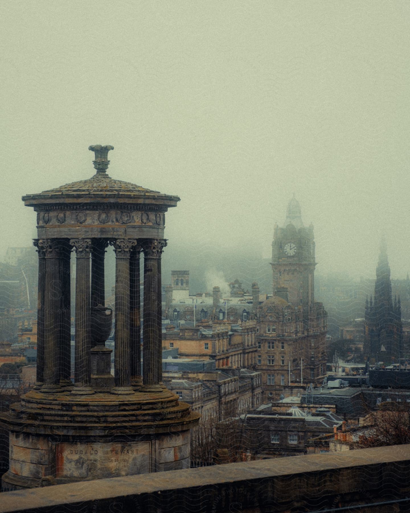 Neoclassical monuments with Corinthian columns and a stone plinth stand out in front, while a misty cityscape, including an ornate clock tower, appears in the background.