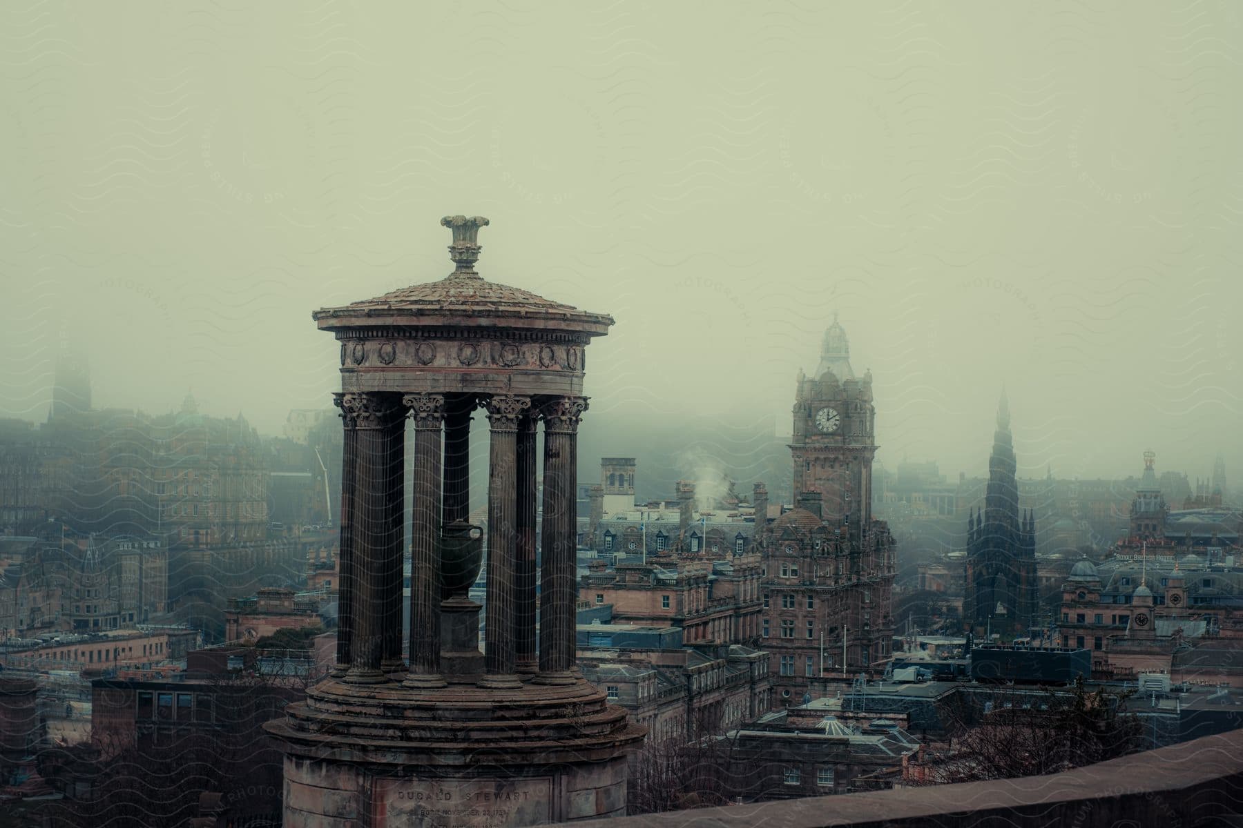 Aerial of a misty historic city, with a classical monument in the foreground and ancient buildings in the background, evoking a sense of mystery and architectural beauty.