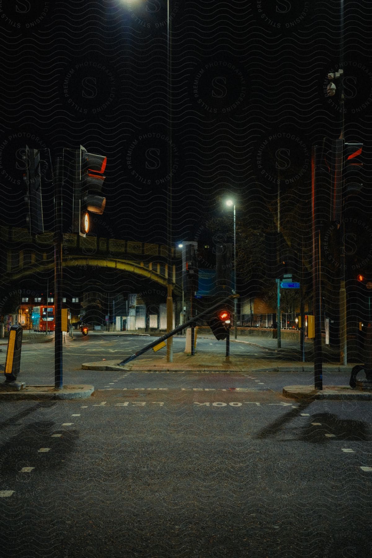 A desolate urban intersection at night, lit by streetlights and devoid of traffic. Traffic lights display red light, indicating stop in all directions.