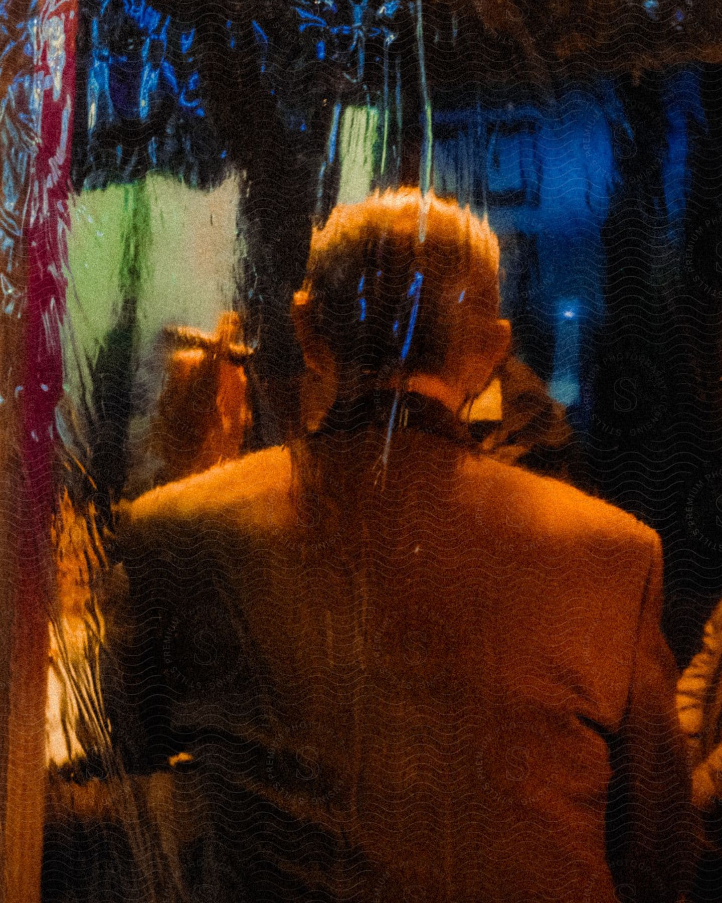 Rear view of a man sitting holding a cigar indoors at night.