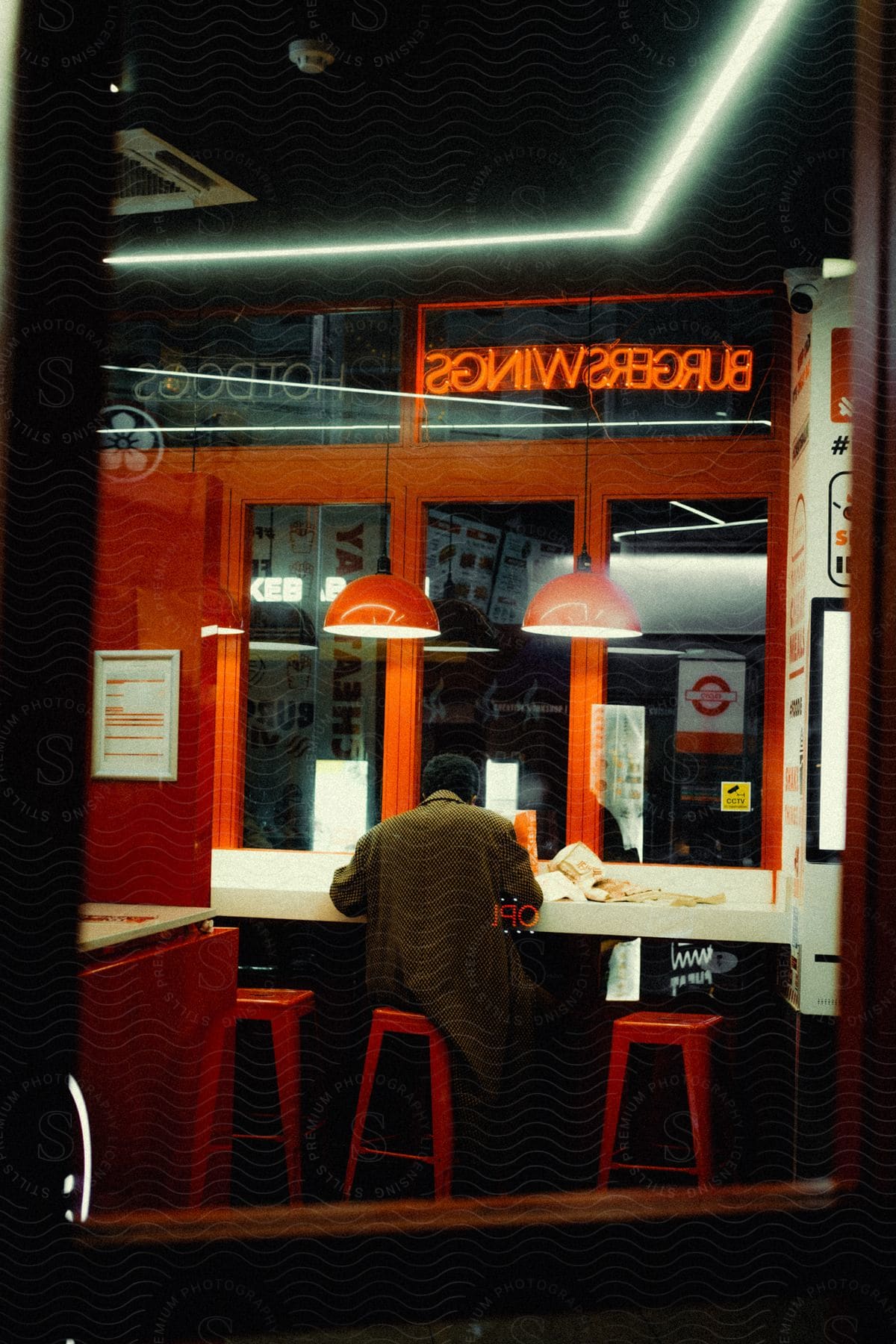 View of a man sitting on a red chair in a burger restaurant at night