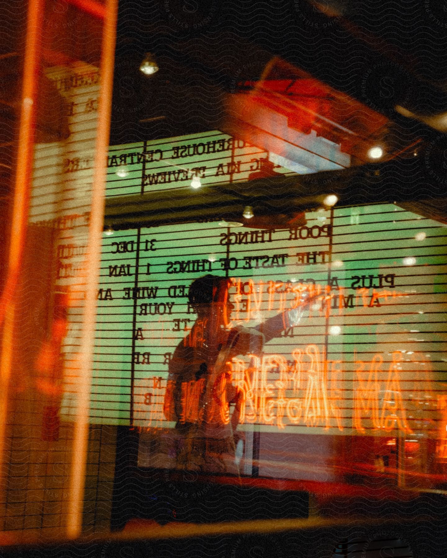 Man pointing his hand at a menu on a backlit wall inside a neon-lit restaurant at night.