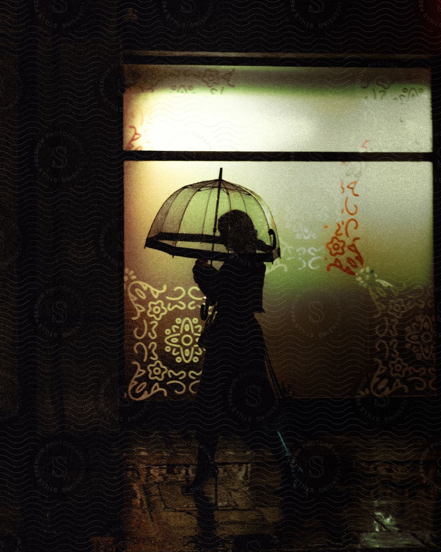 Stock photo of silhouette of a woman walking down a dark street in the city at night, using an umbrella and high-heeled leather boots.