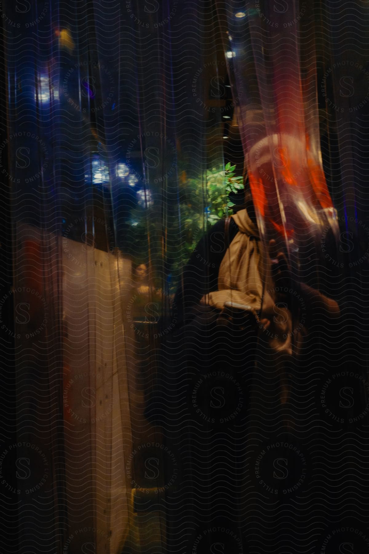 A person coming out through a transparent curtain that is reflecting some lights from the environment and it is at night