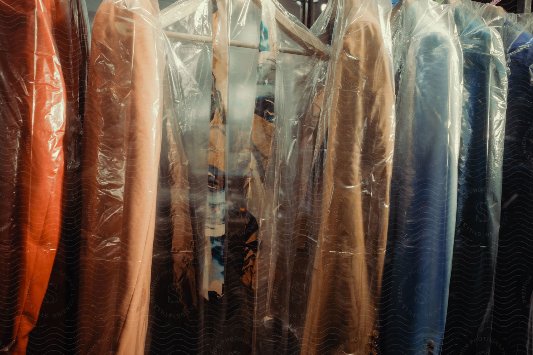 Close-up of blazers on hangers of different tones and colors protected by transparent plastic.