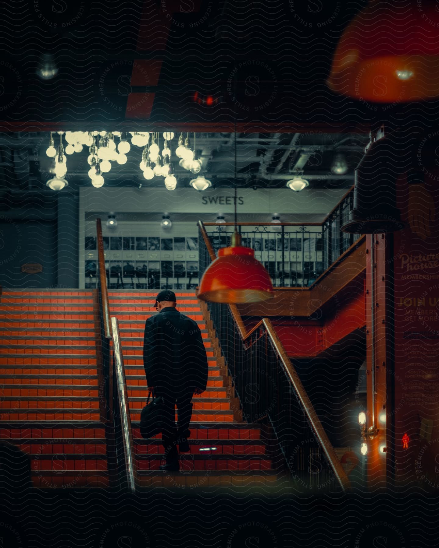 A man holding a bag walks up a staircase leading out of a subway station with series of light shining over the stairs.