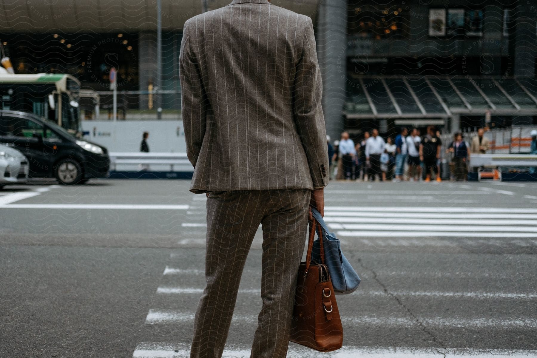 A woman in a business suit carry a bag and purse standing at a crosswalk