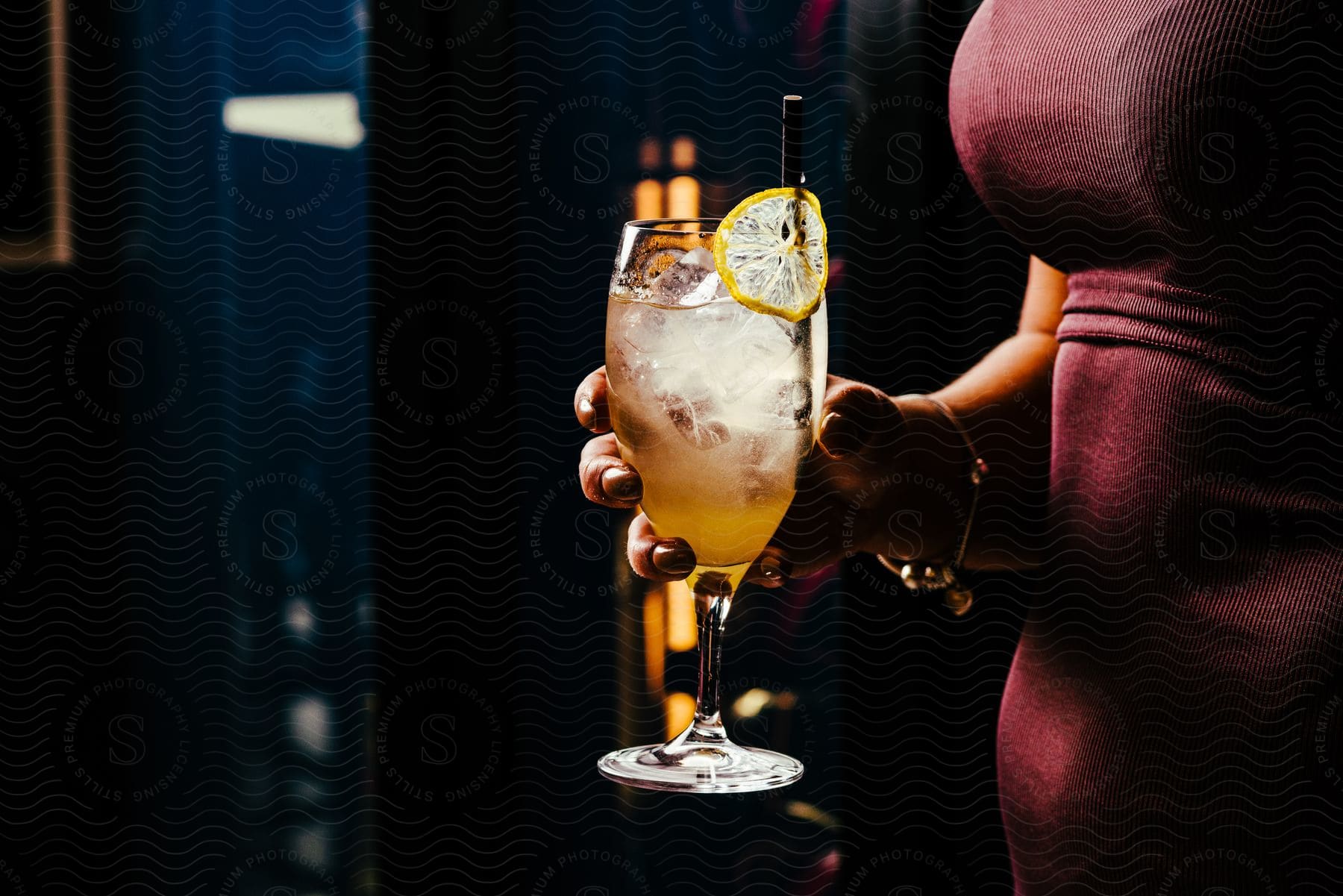 The hand holds a refreshing cocktail with a slice of lemon as a garnish.