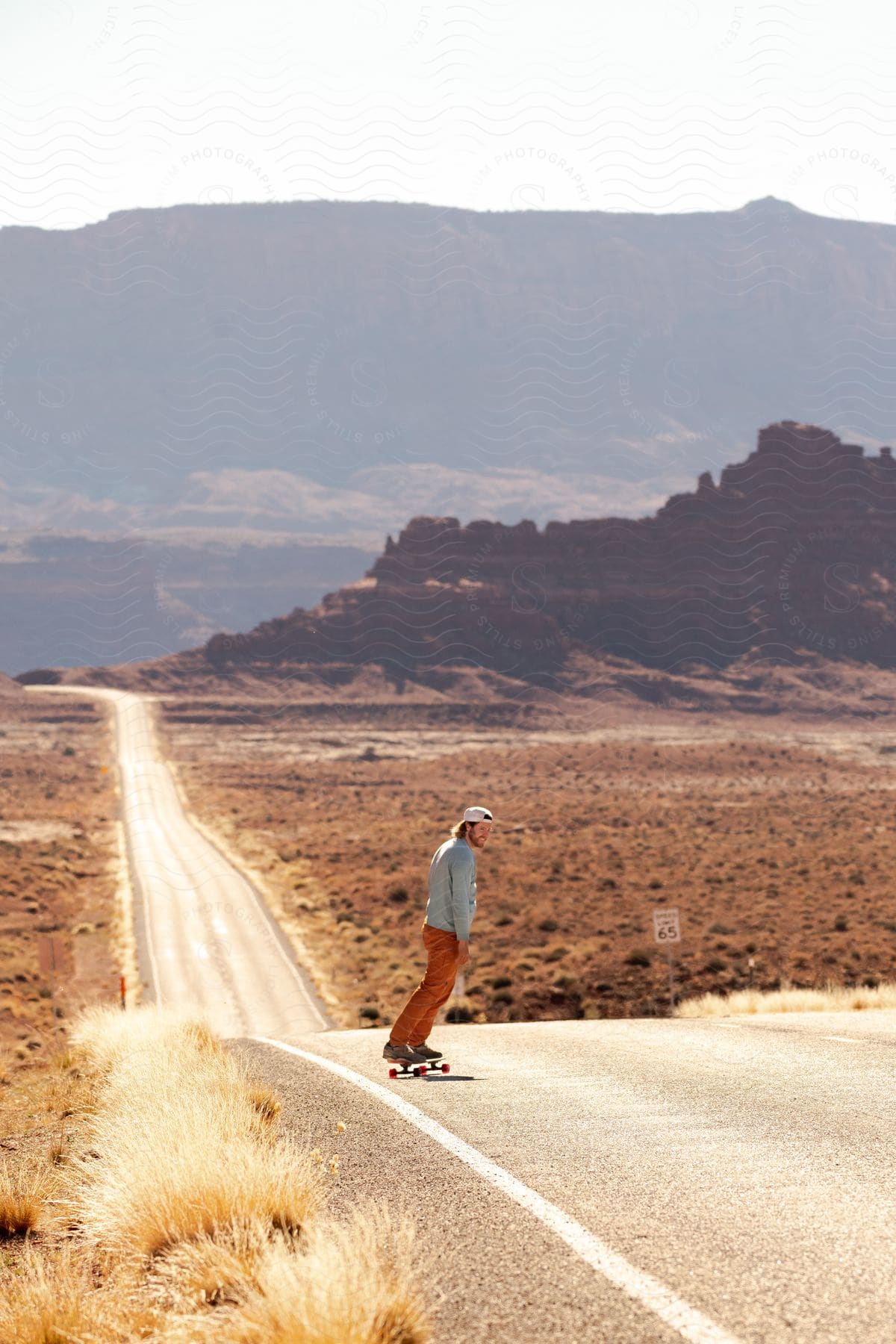Man riding a skateboard up a hill on a rural road with mountains in the distance