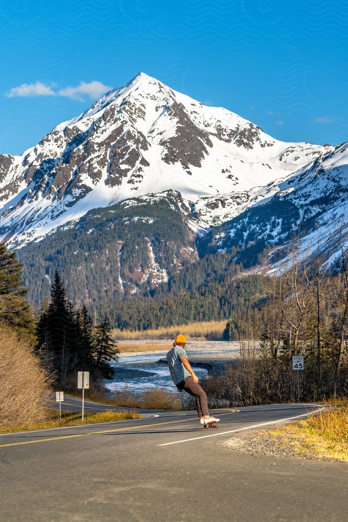 Man riding a skateboard on an asphalt with snowy forests and mountains during the day