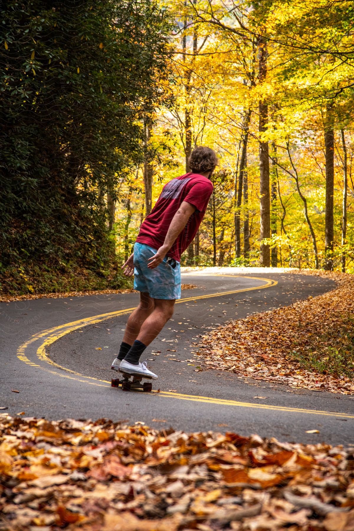 A skateboarder skating along a winding forest road.