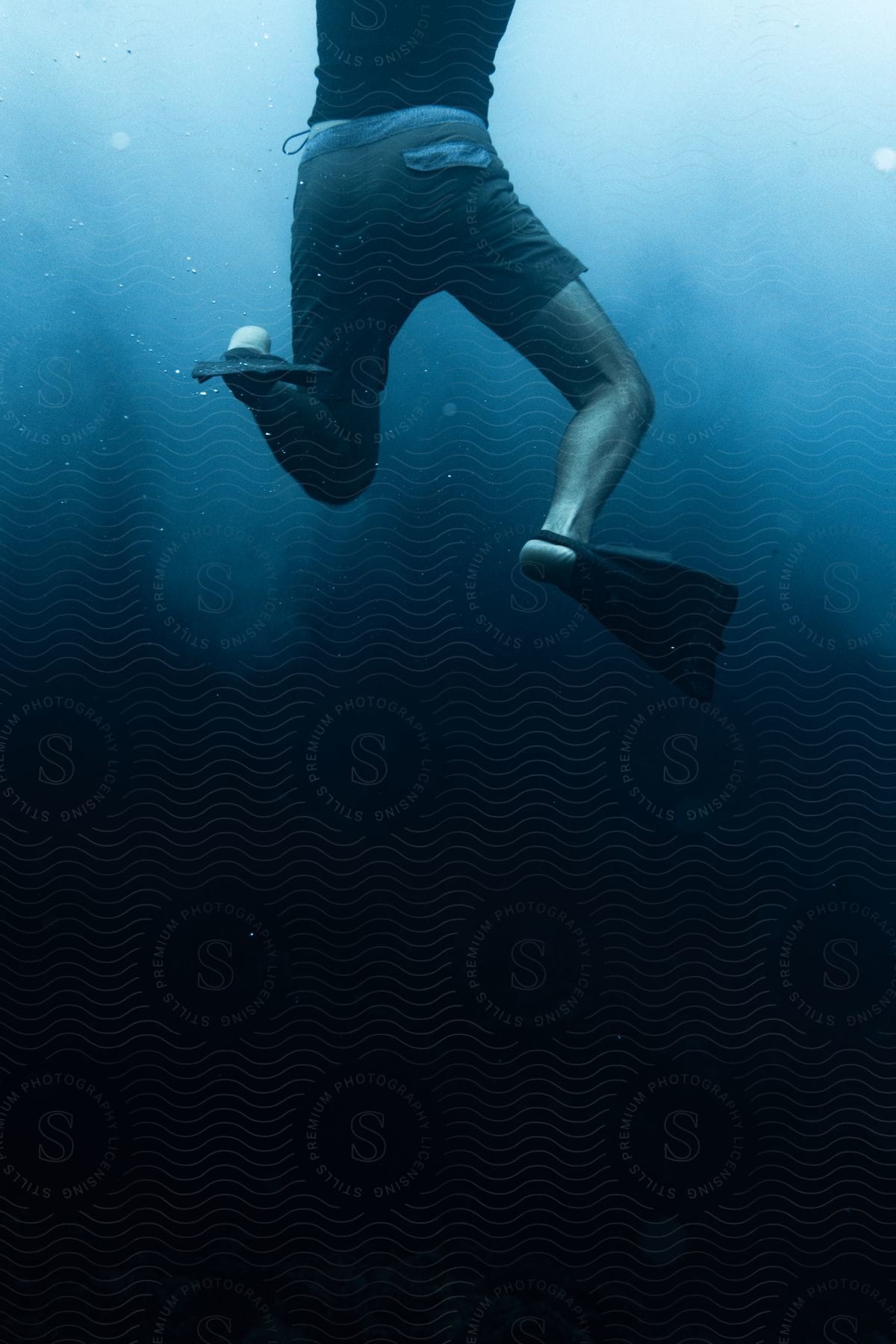 Stock photo of person diving into deep blue water with fins, only lower half visible.